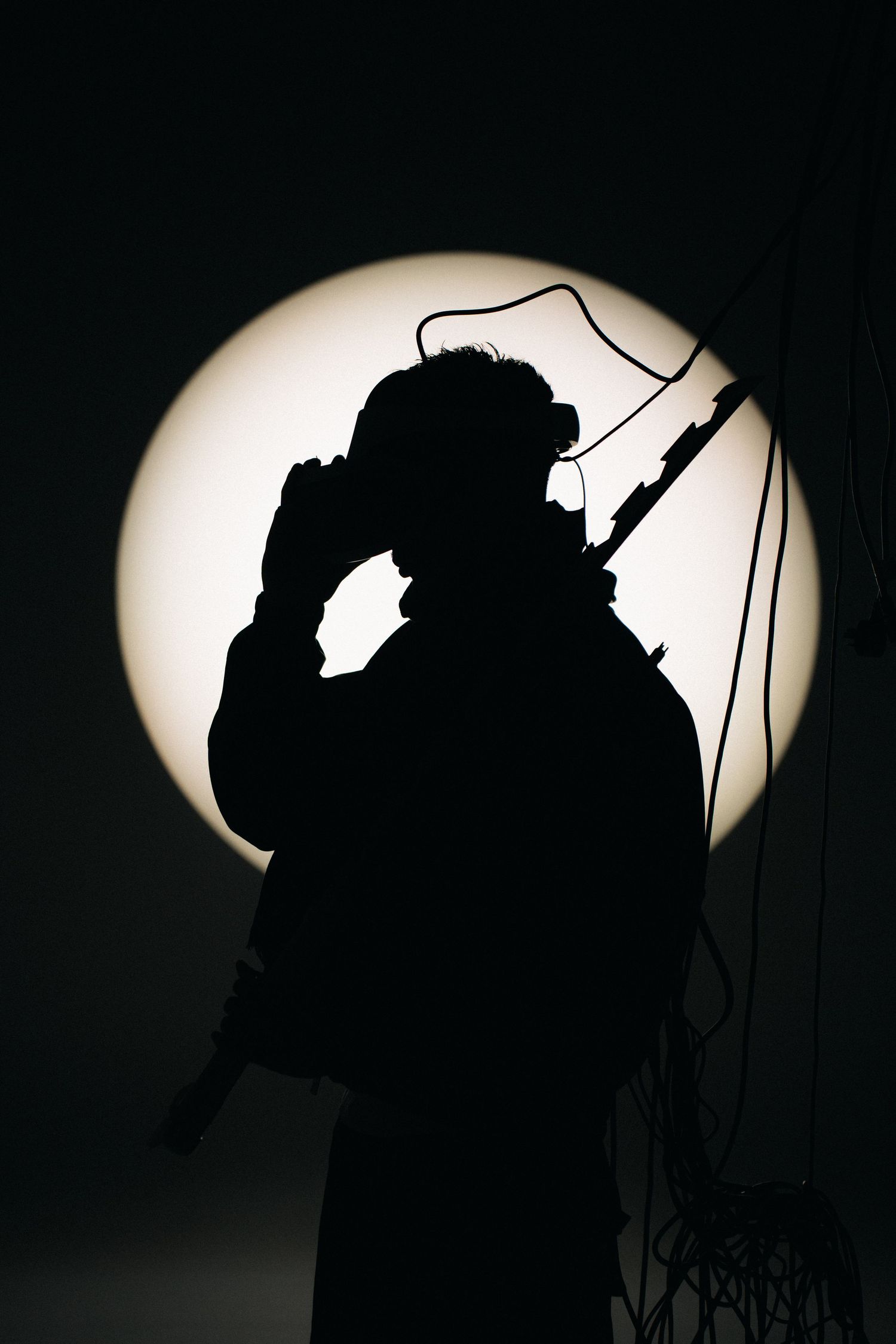 Silhouetted figure with microphone against circular light backdrop.