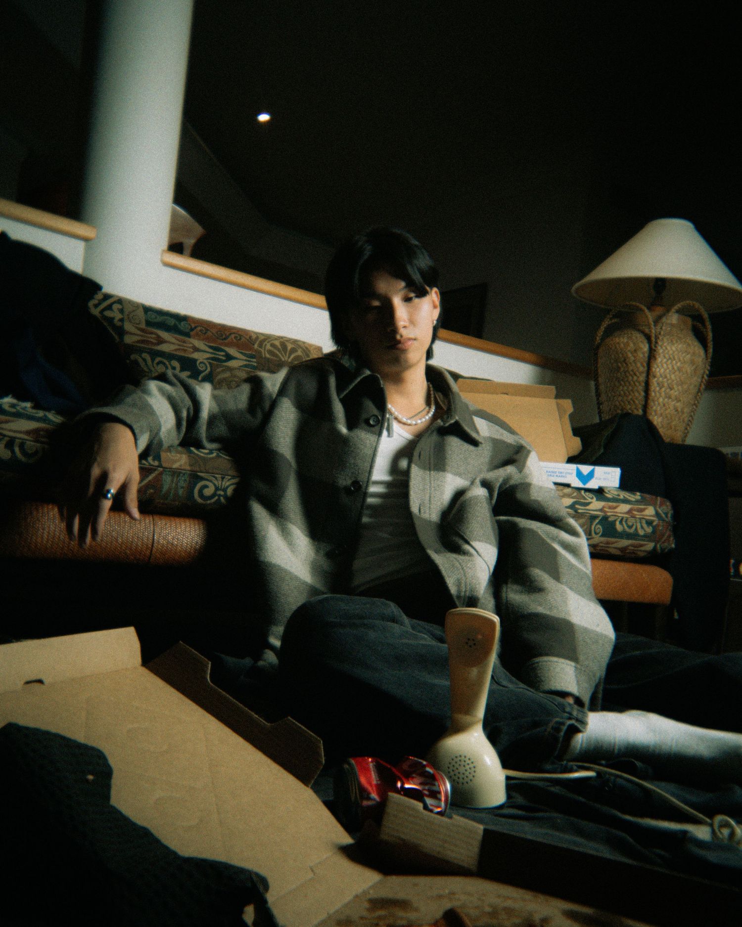 Person sits in moody lighting on couch wearing casual streetwear and white socks in a dimly lit room.