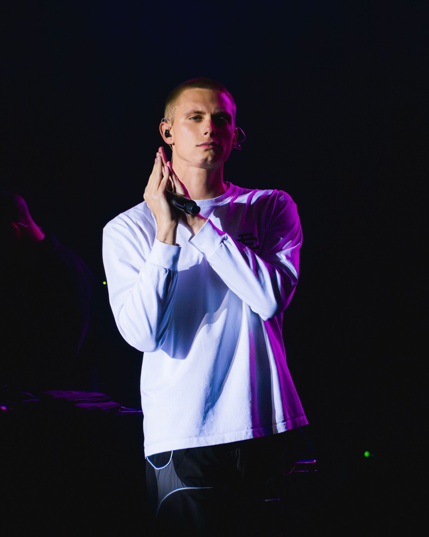 Concert performer in white shirt illuminated by purple stage lighting during emotional performance.