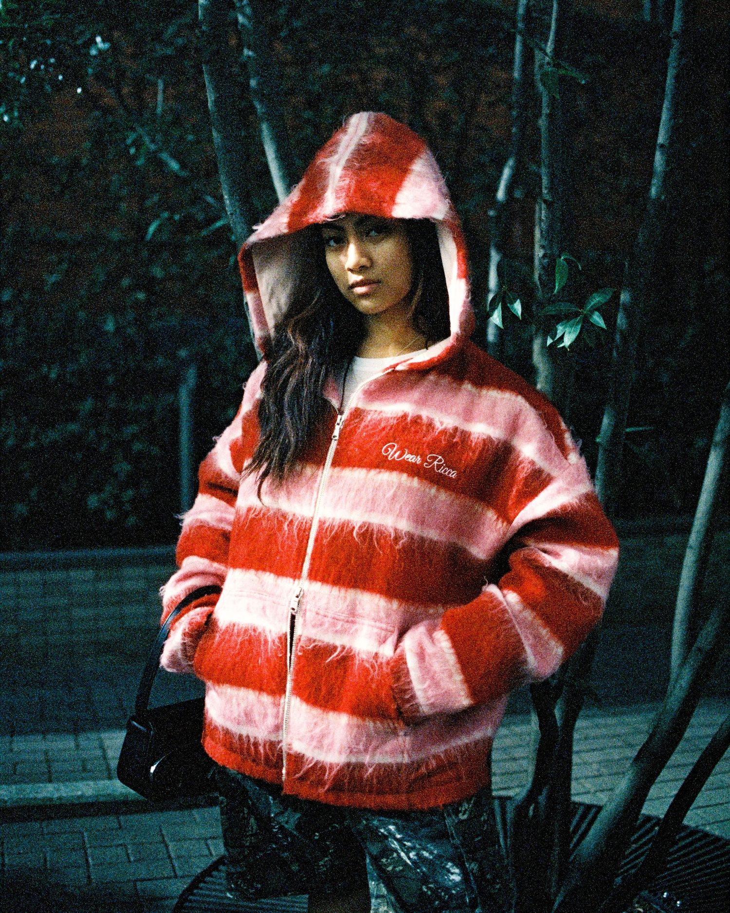 Person wearing striped red and white hooded jacket posing against dark background.