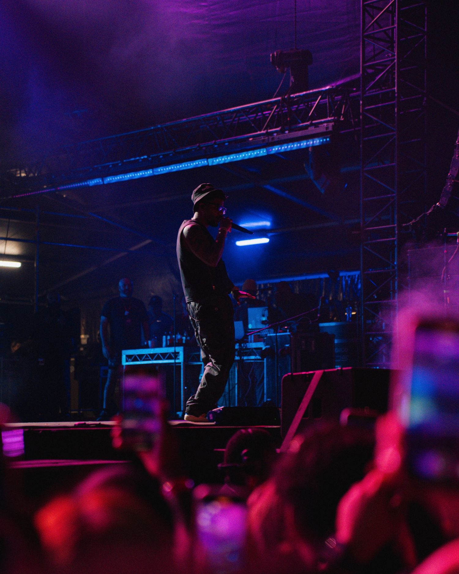 Concert performer silhouetted on stage with purple and blue lighting while crowd watches at nighttime music venue.