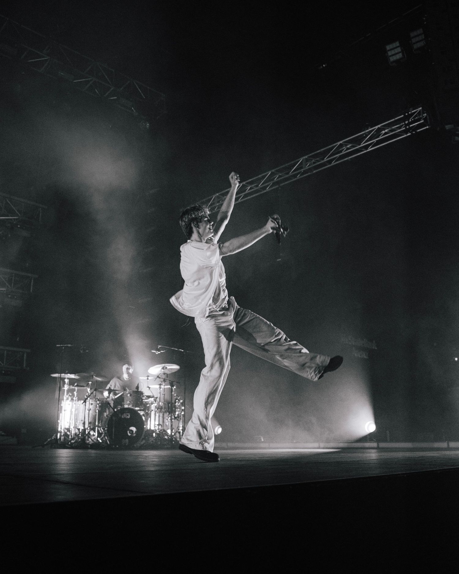 A dynamic stage performance in black and white shows a performer leaping high in the air with dramatic backlighting and fog.