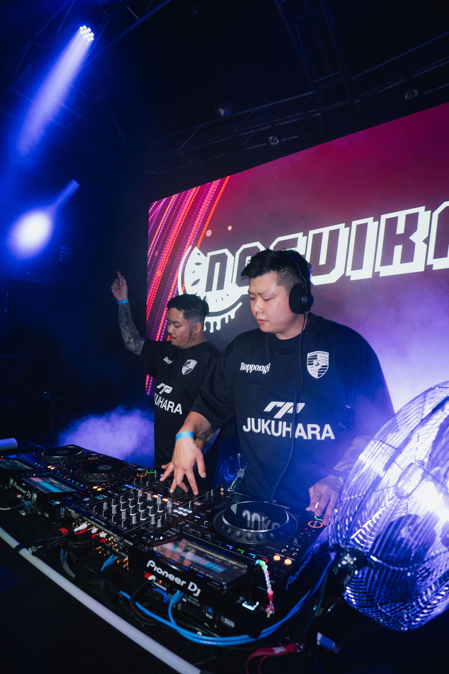 DJs performing at club event with blue lighting and equipment display.