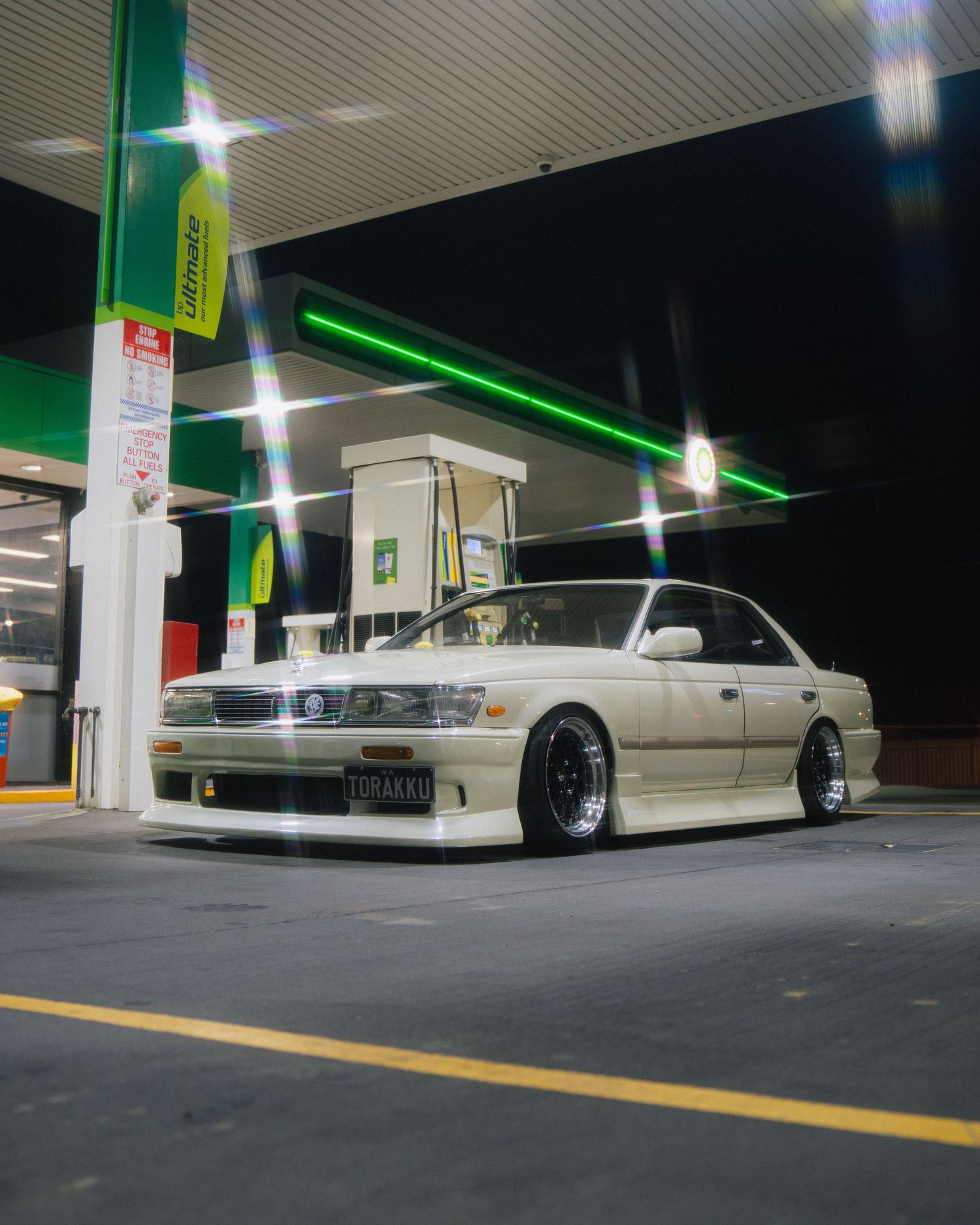 Lowered silver sports car parked at a gas station at night with custom wheels and body kit.
