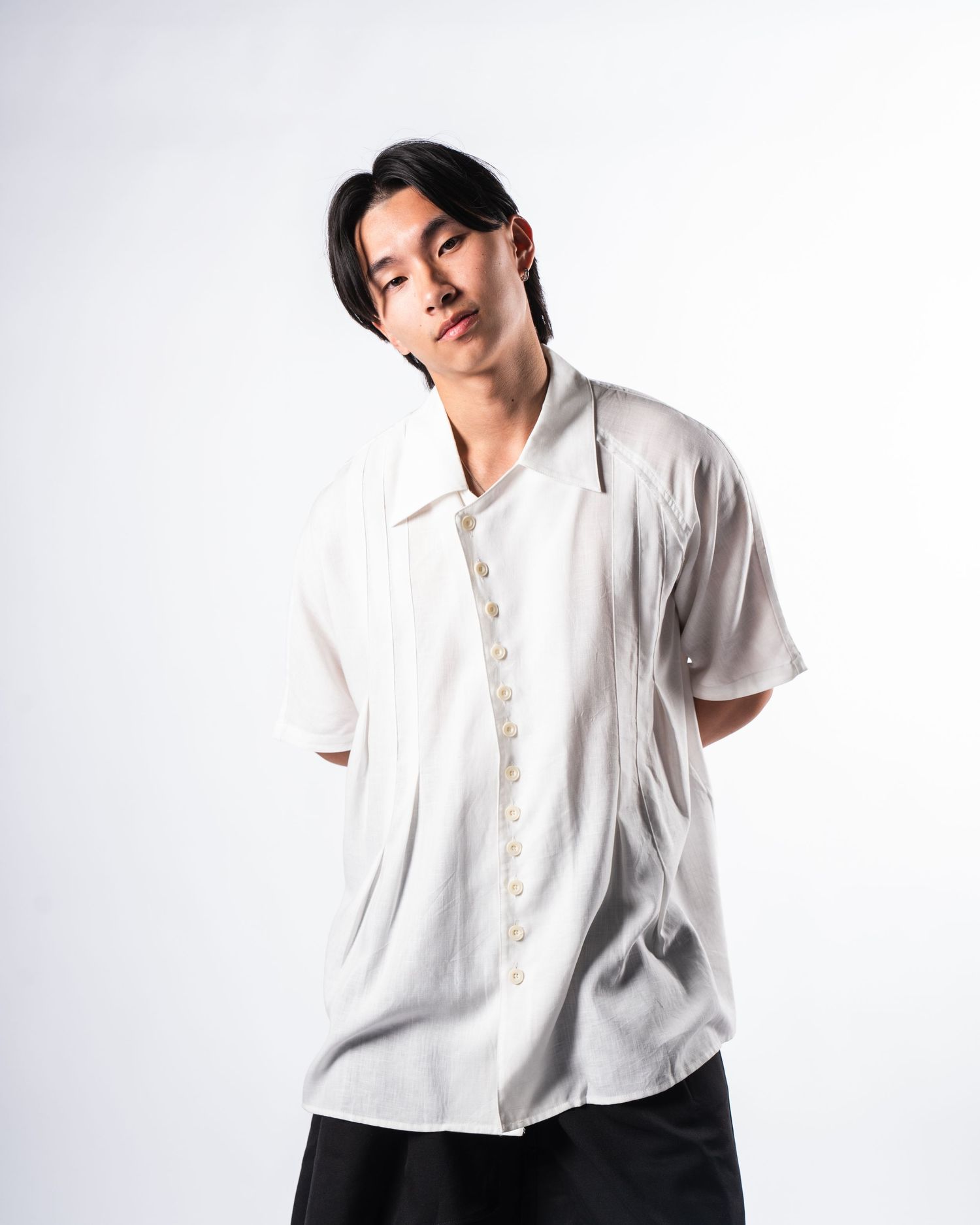 Person in loose white button-up shirt posing against light background.