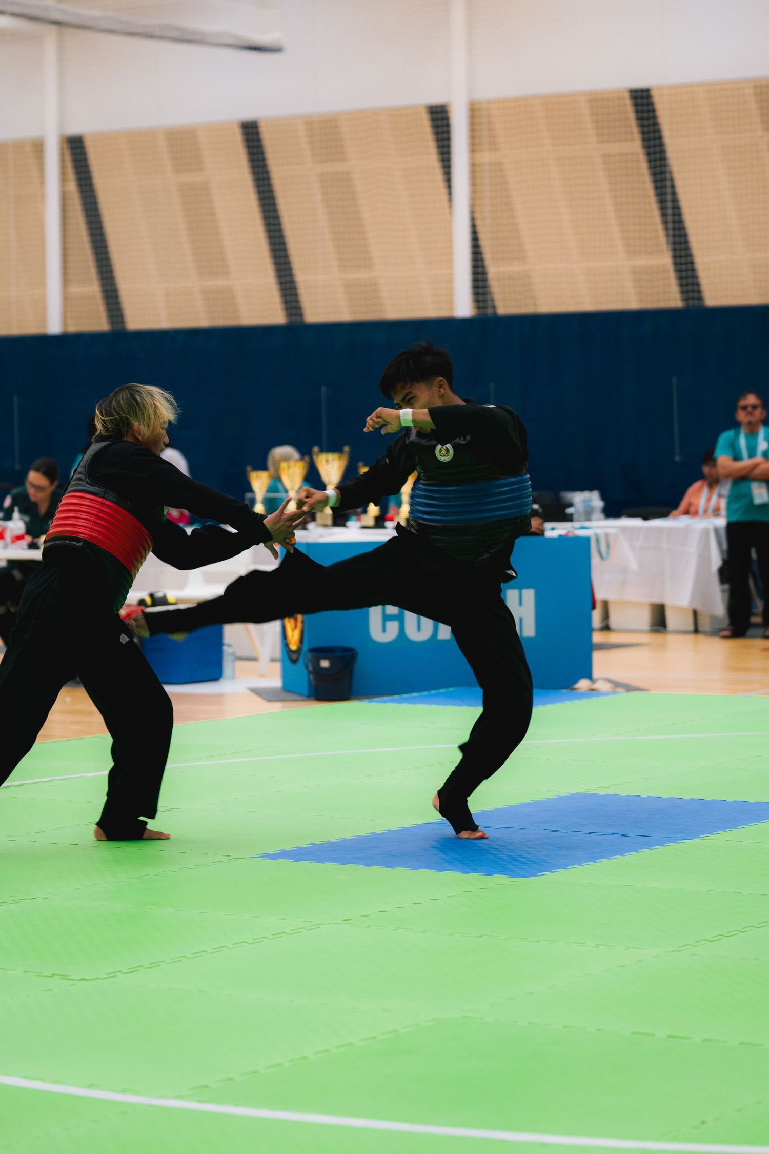 Two martial artists in black uniforms perform high kicks during competition.
