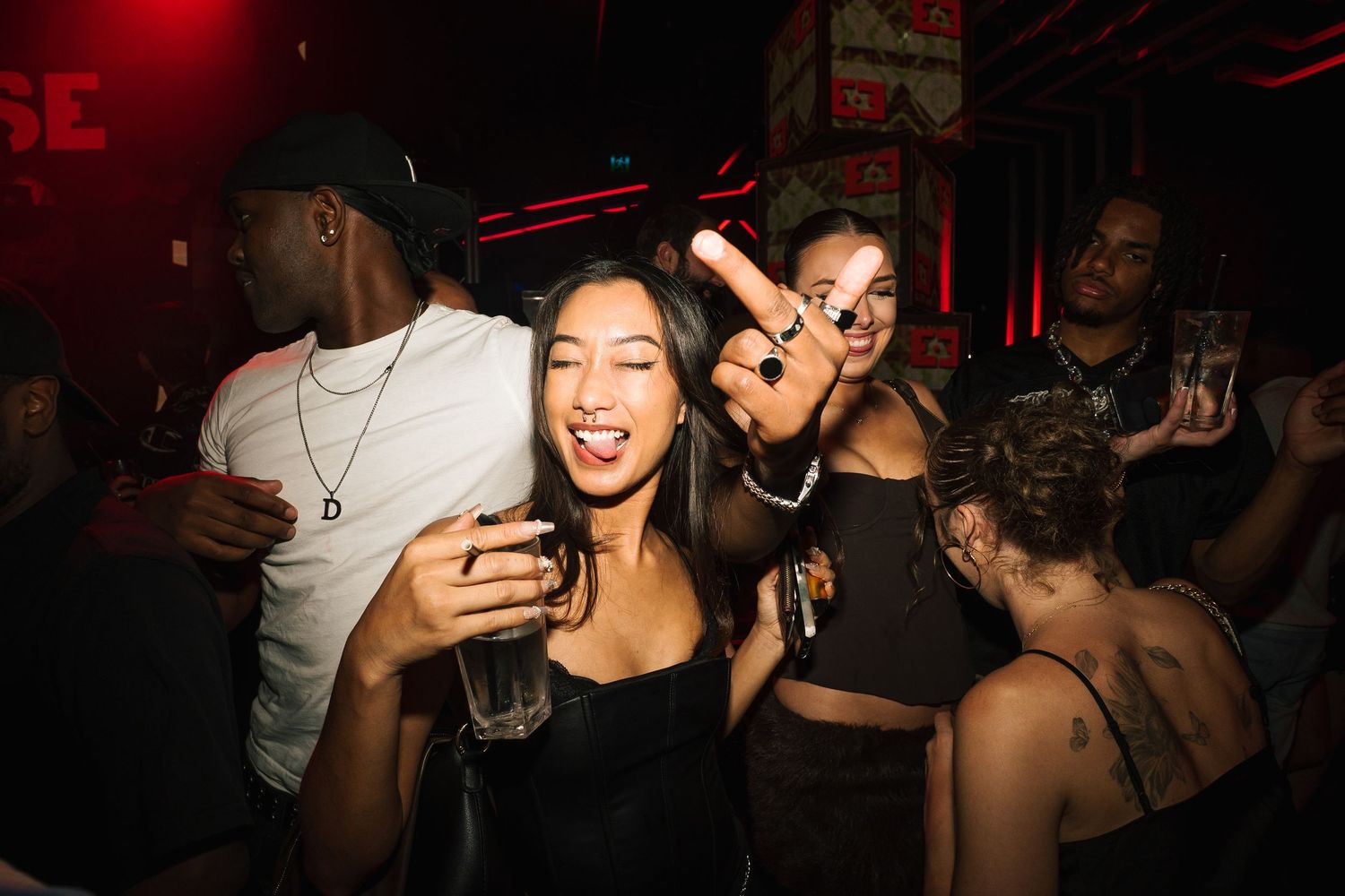 People dancing and socializing at a nightclub with red lighting and dark atmosphere.