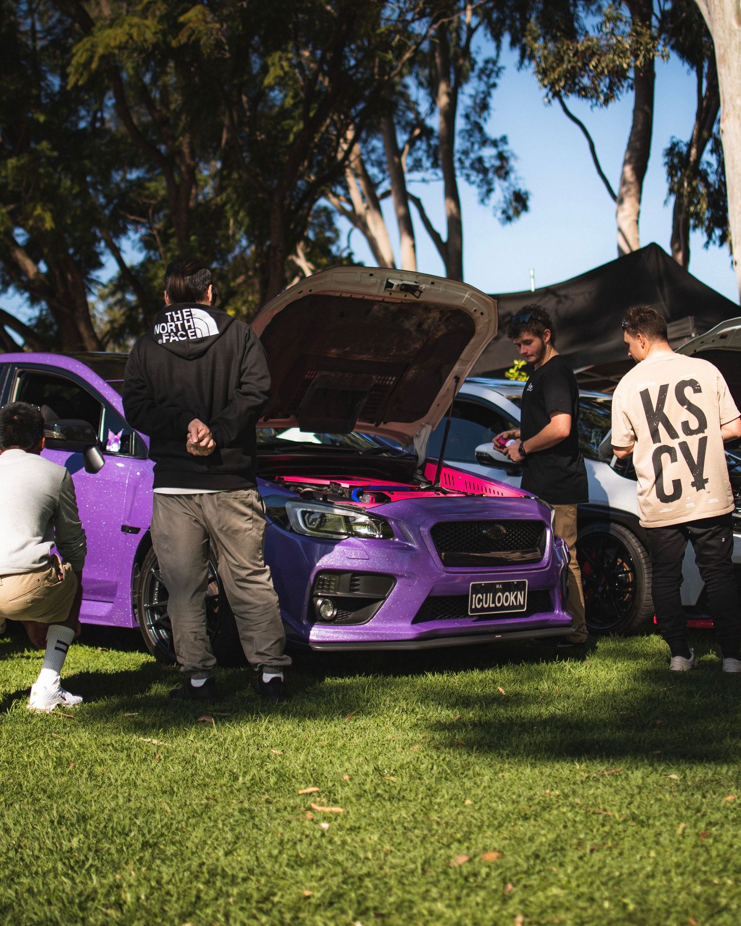 Custom Subaru vehicles lined up for display on grassy field with event banner.