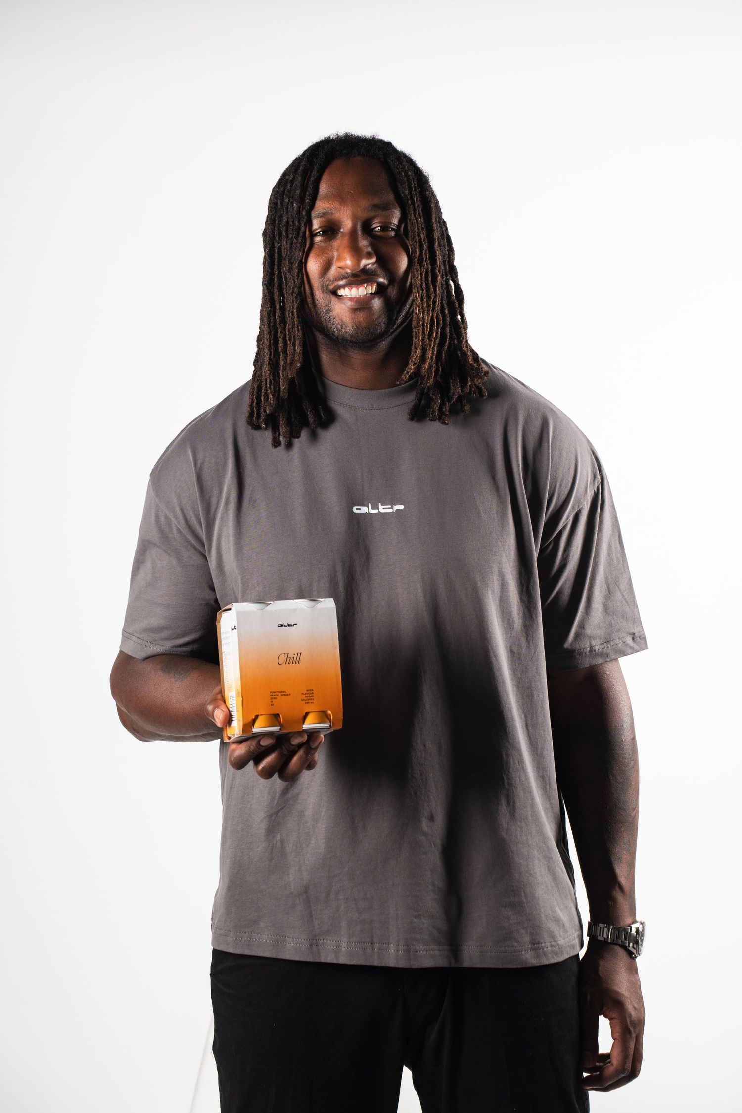 Person in grey t-shirt holding orange beverage against white background.