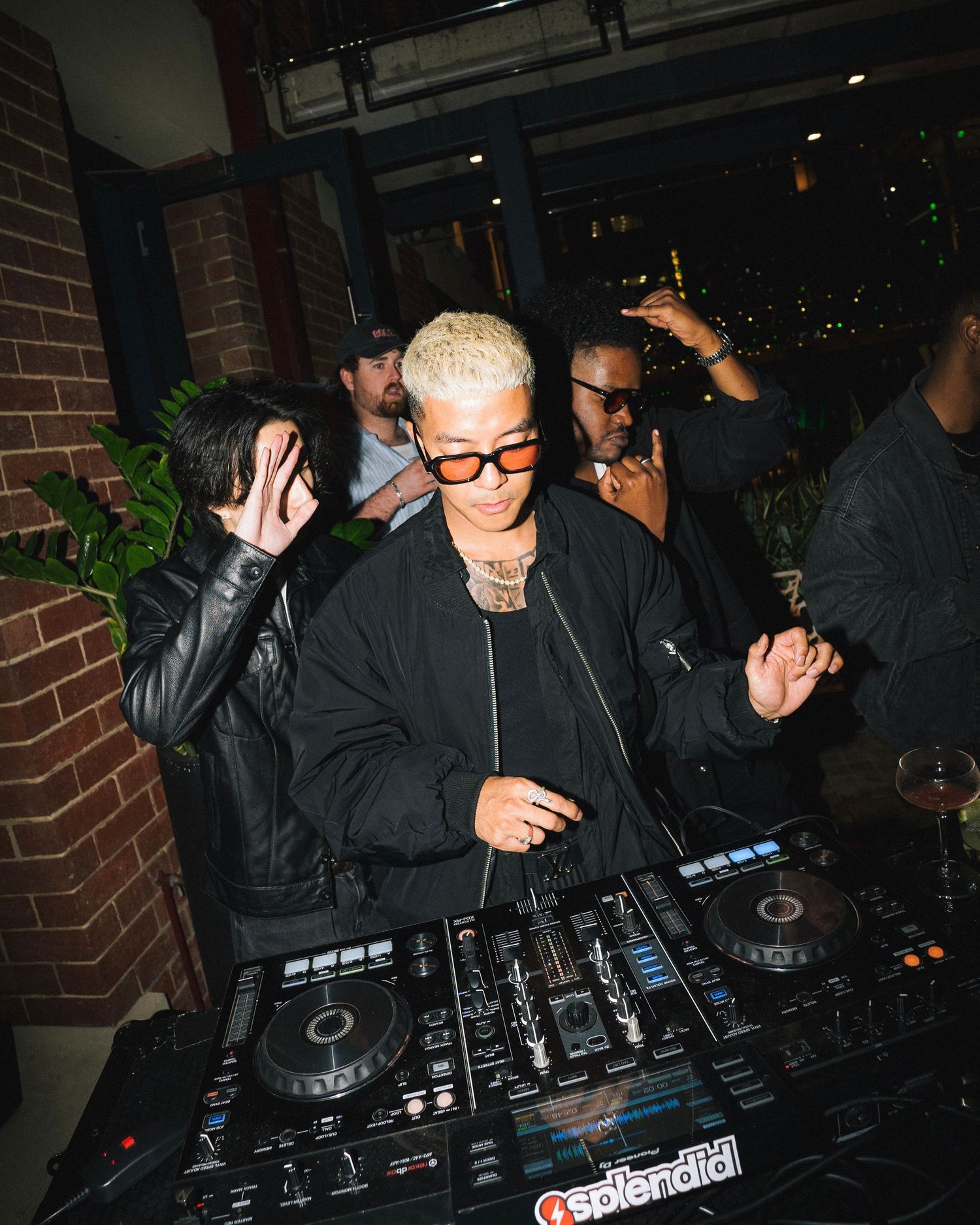 DJ performing at dark venue with brick walls and mixing equipment.