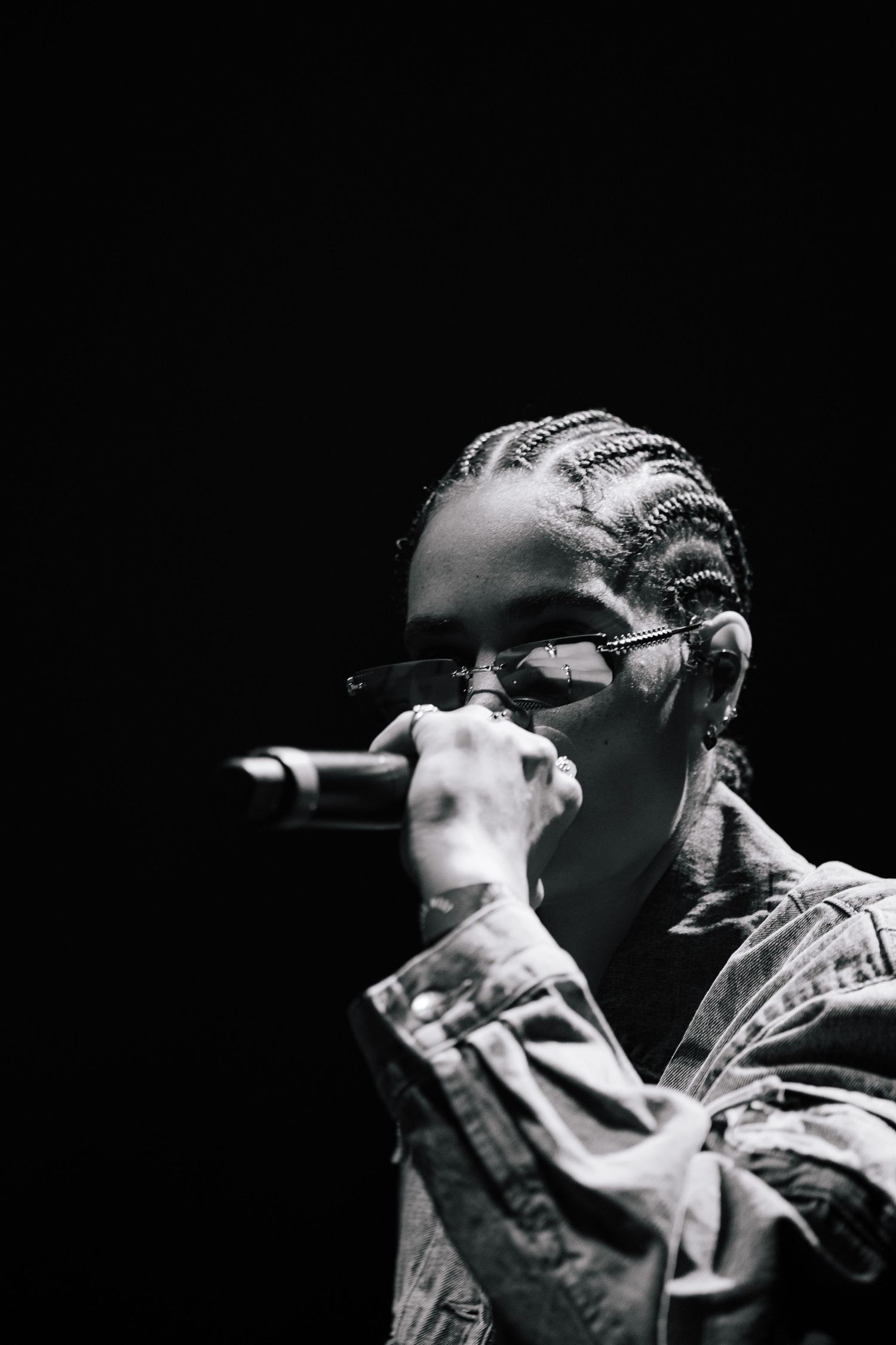 Black and white portrait of a performer in glasses holding a microphone during a concert performance.