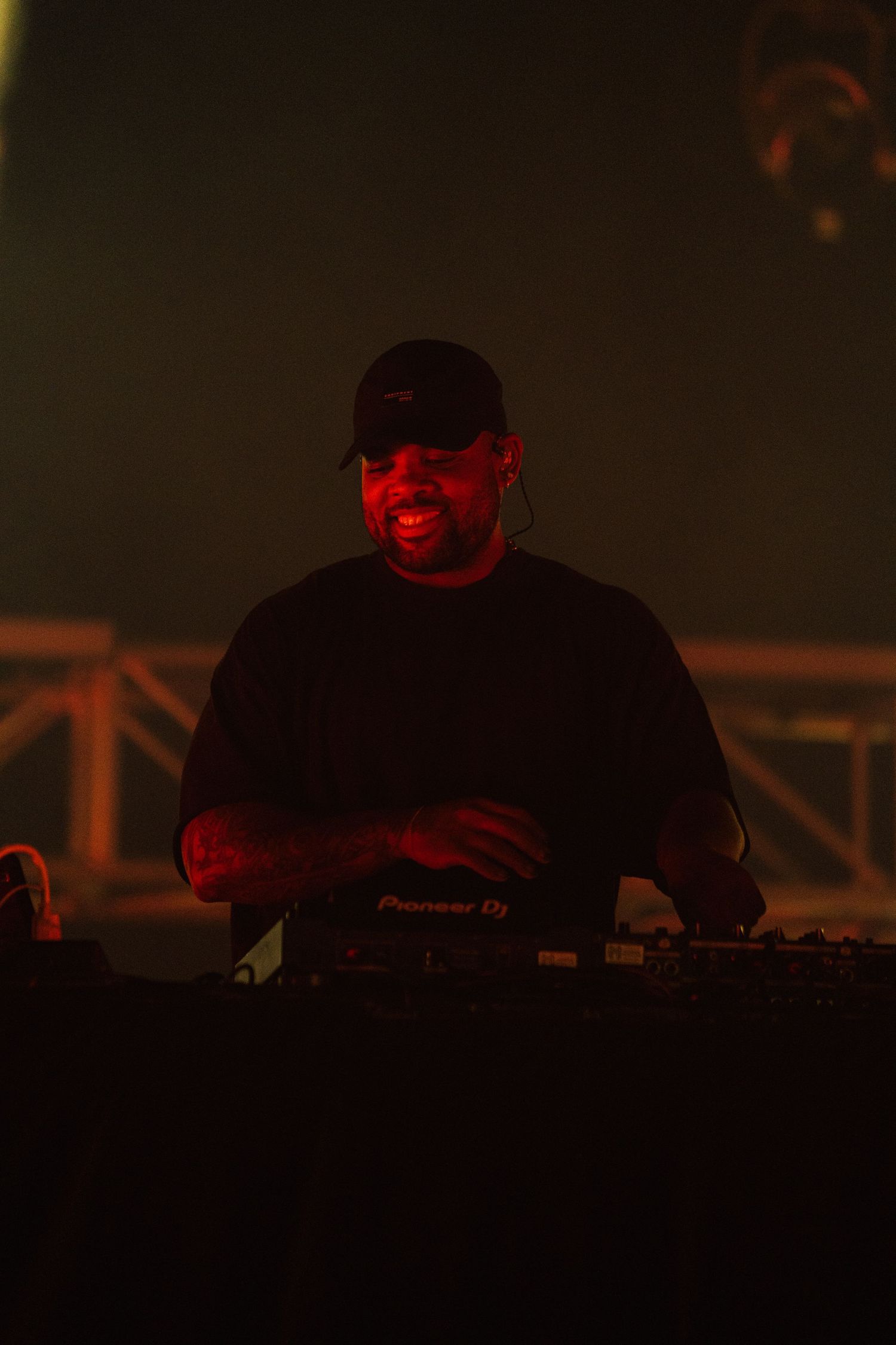 A DJ performs at a dimly lit venue bathed in red lighting while standing behind equipment at night.