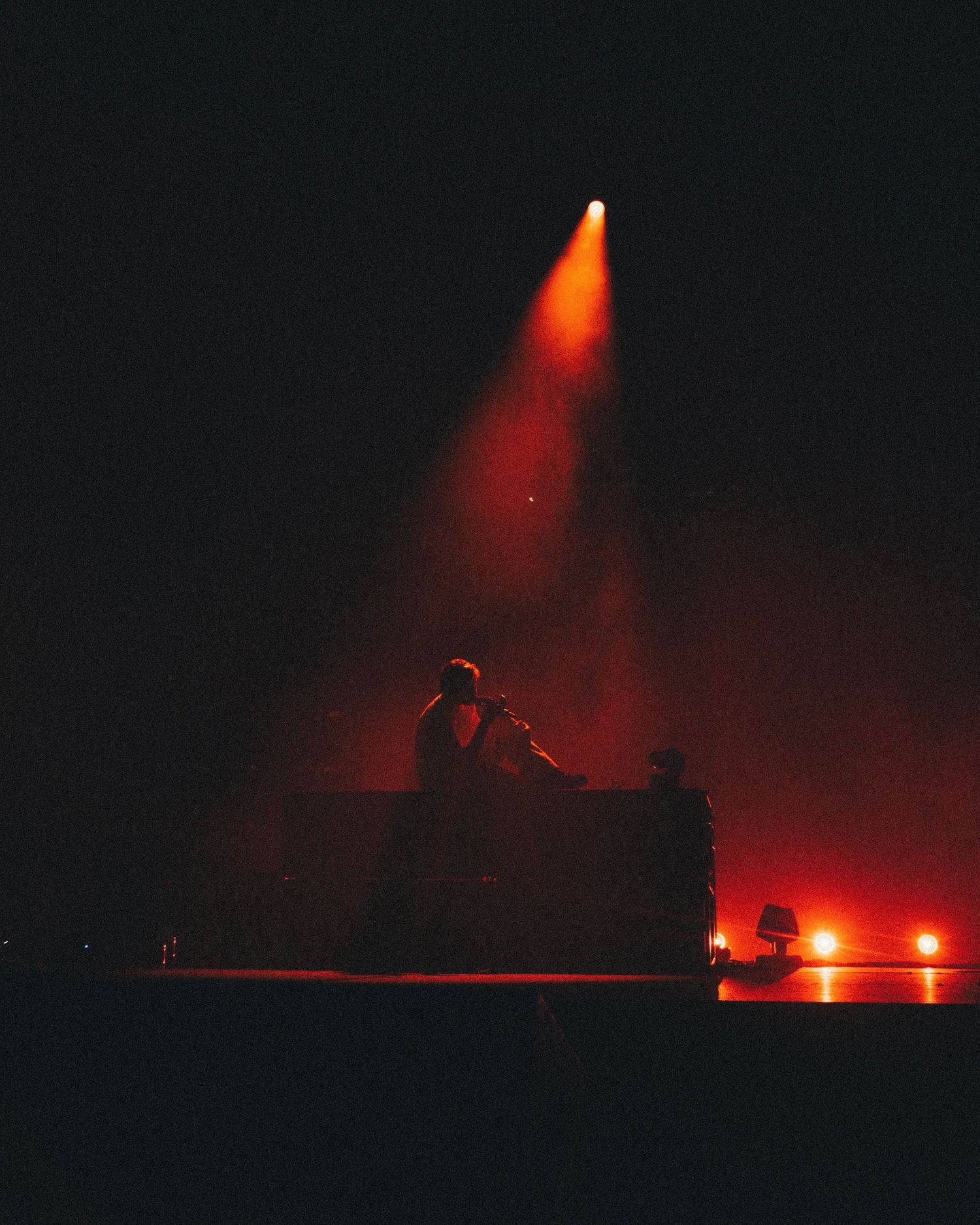 Silhouette of DJ performing on dark stage with dramatic red spotlight and atmospheric fog effects.