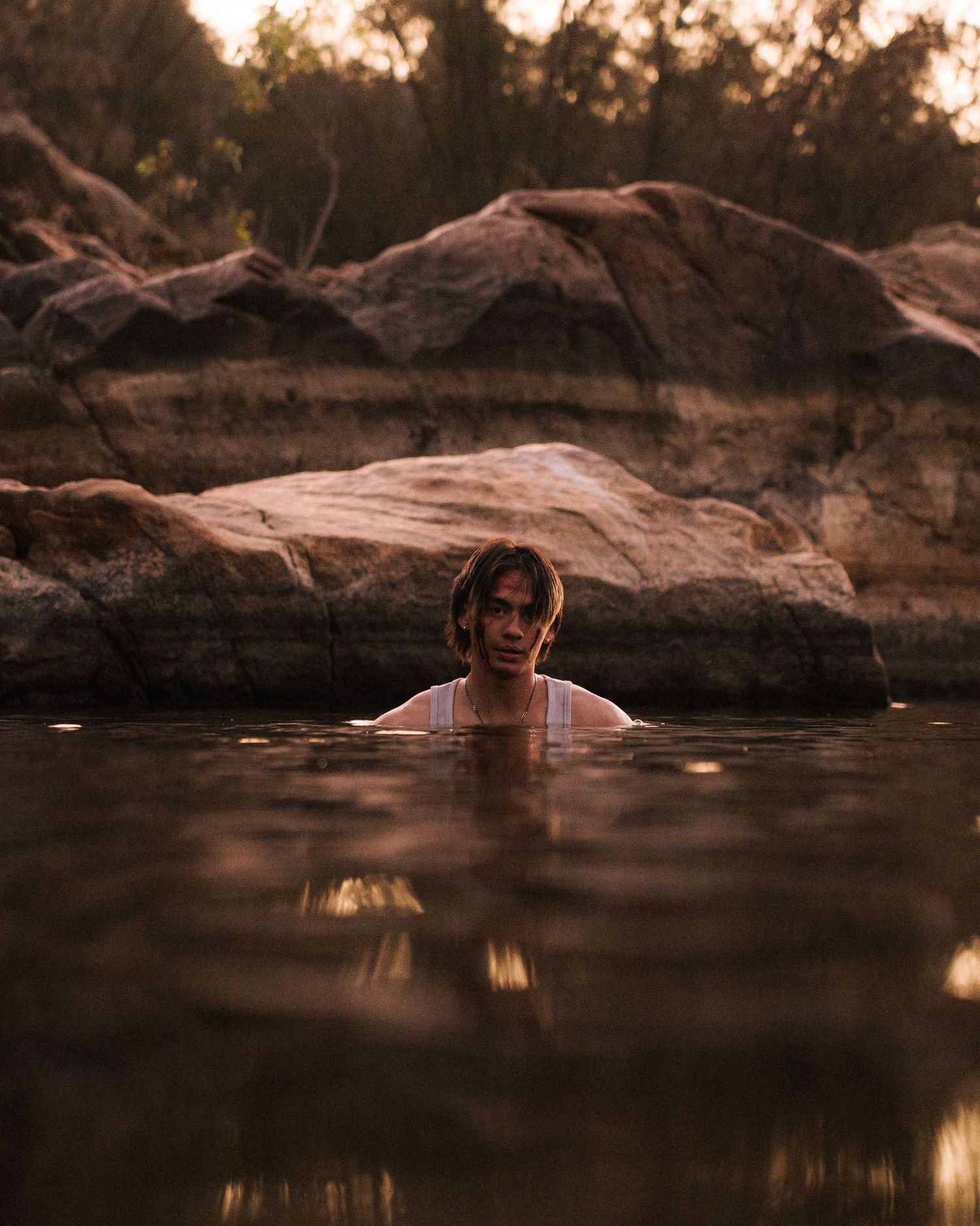 Someone swimming in dark reflective water surrounded by rocky outcrops at sunset creates a moody scenic atmosphere.