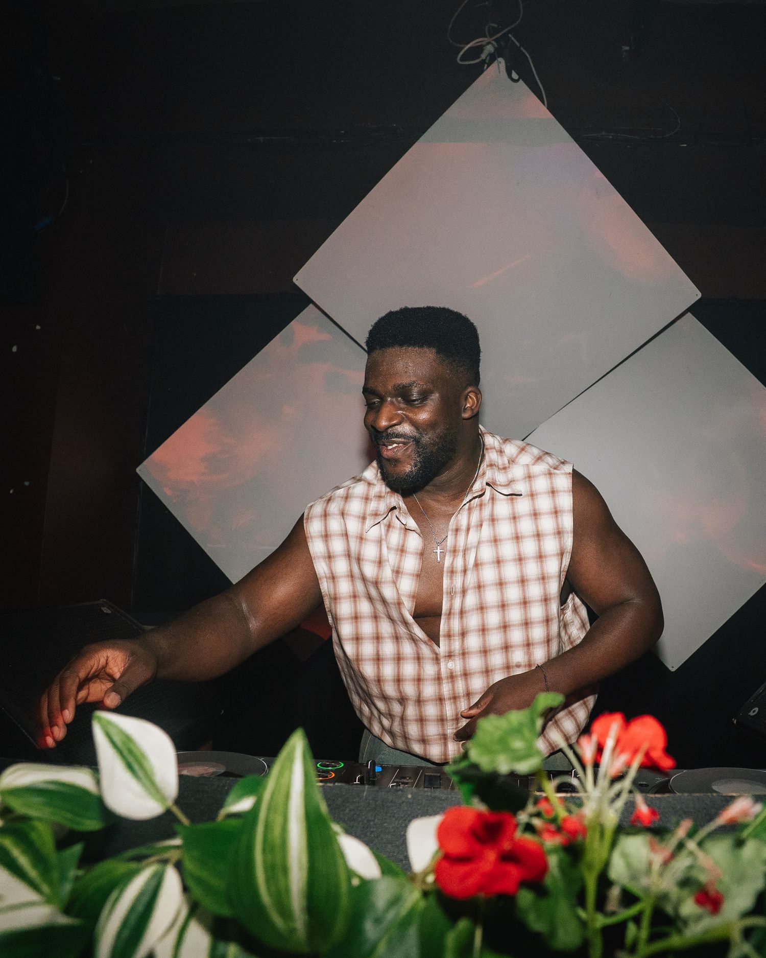 DJ performing behind decks with tropical plants and decorative elements in stylish venue setup.