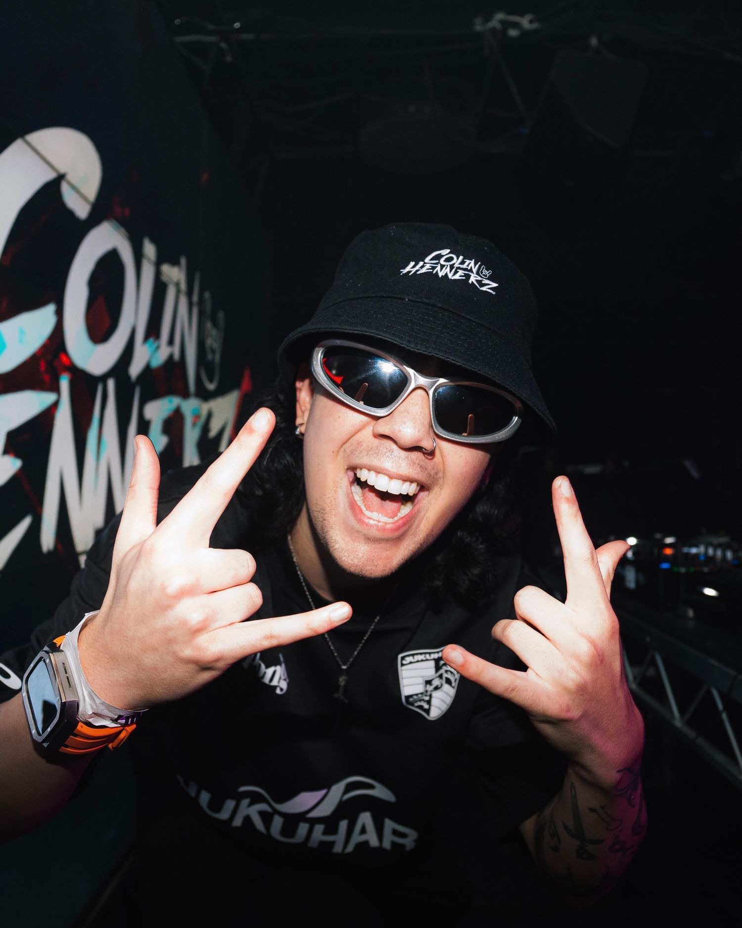 DJ in black cap and sunglasses making rock gesture while performing.