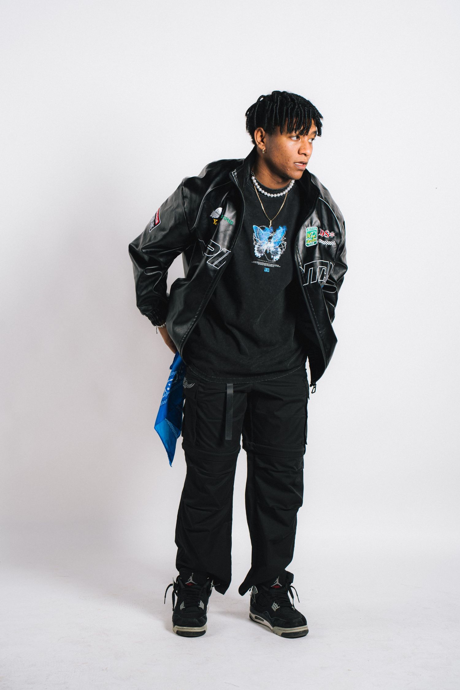 Model wearing a black streetwear outfit with hoodie, cargo pants and sneakers against white background.