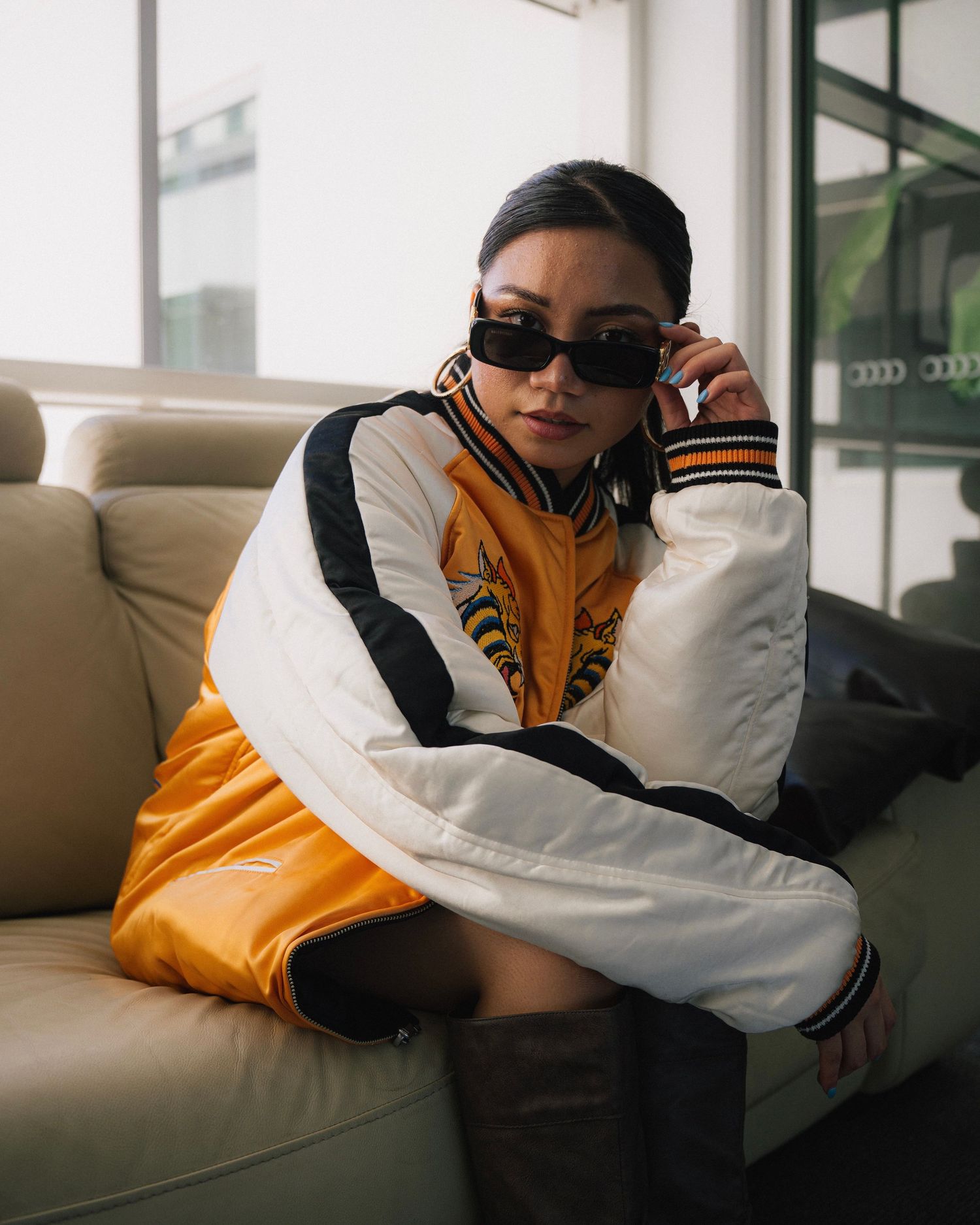 Stylish portrait of a person in orange and white jacket relaxing on beige couch.