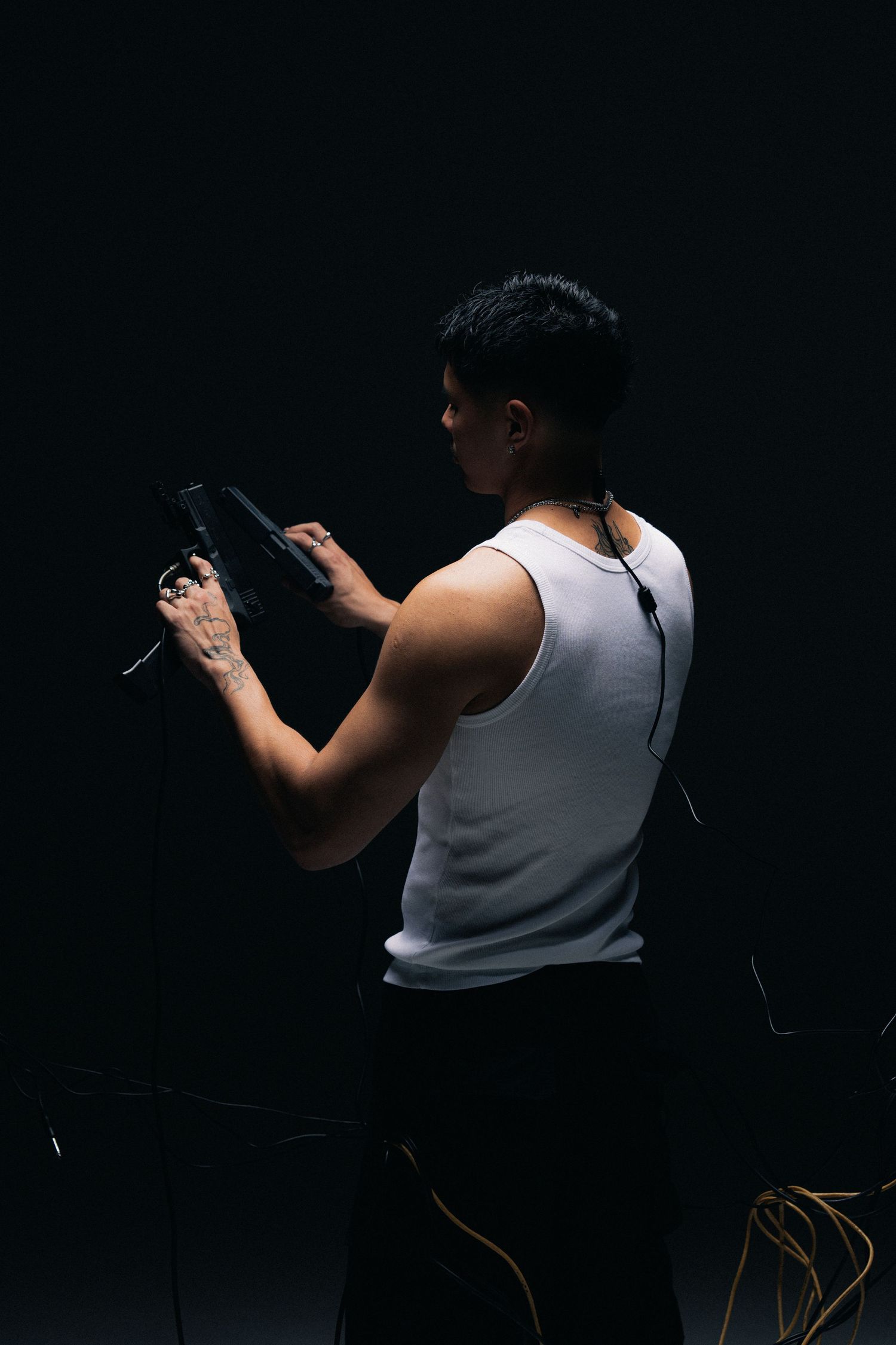 Dramatic side view of person in white tank top holding dual pistols against dark background.