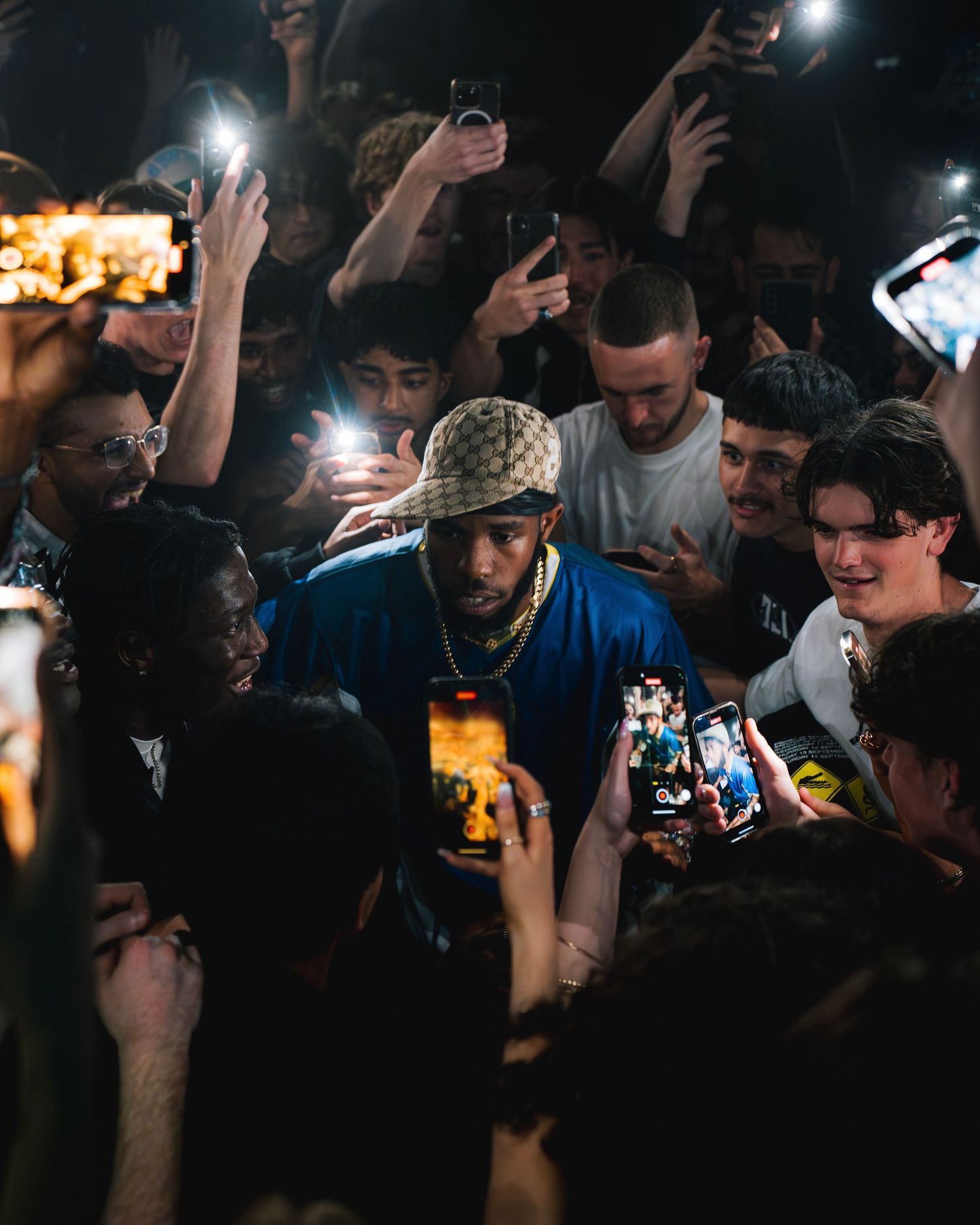 Crowd surrounds performer as fans hold up phones to capture moment at concert venue.