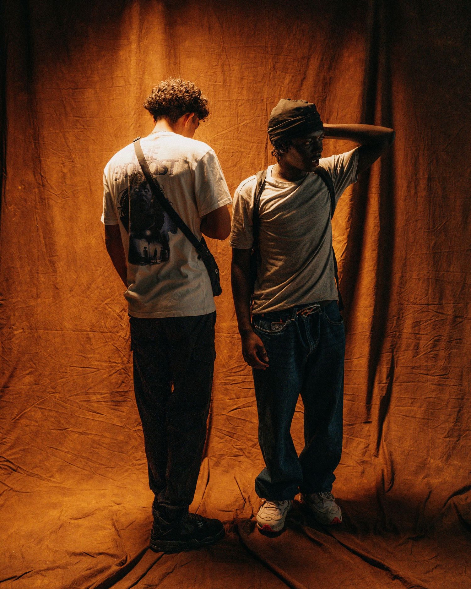 Two people standing in front of a brown backdrop with dramatic lighting pose in casual attire.