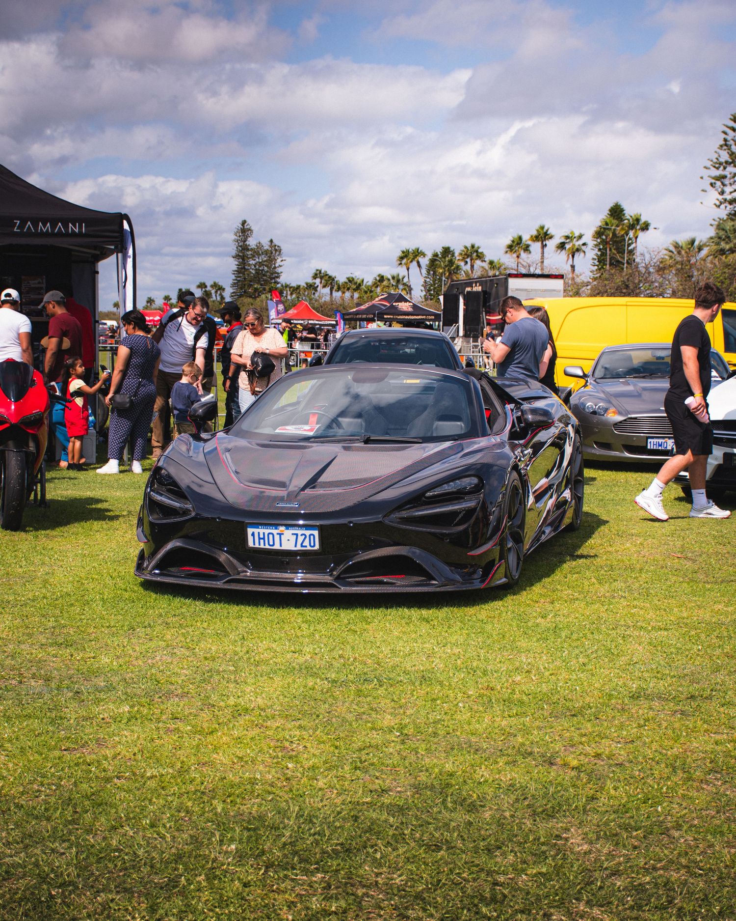 Black McLaren supercar on display at outdoor car event with crowd.