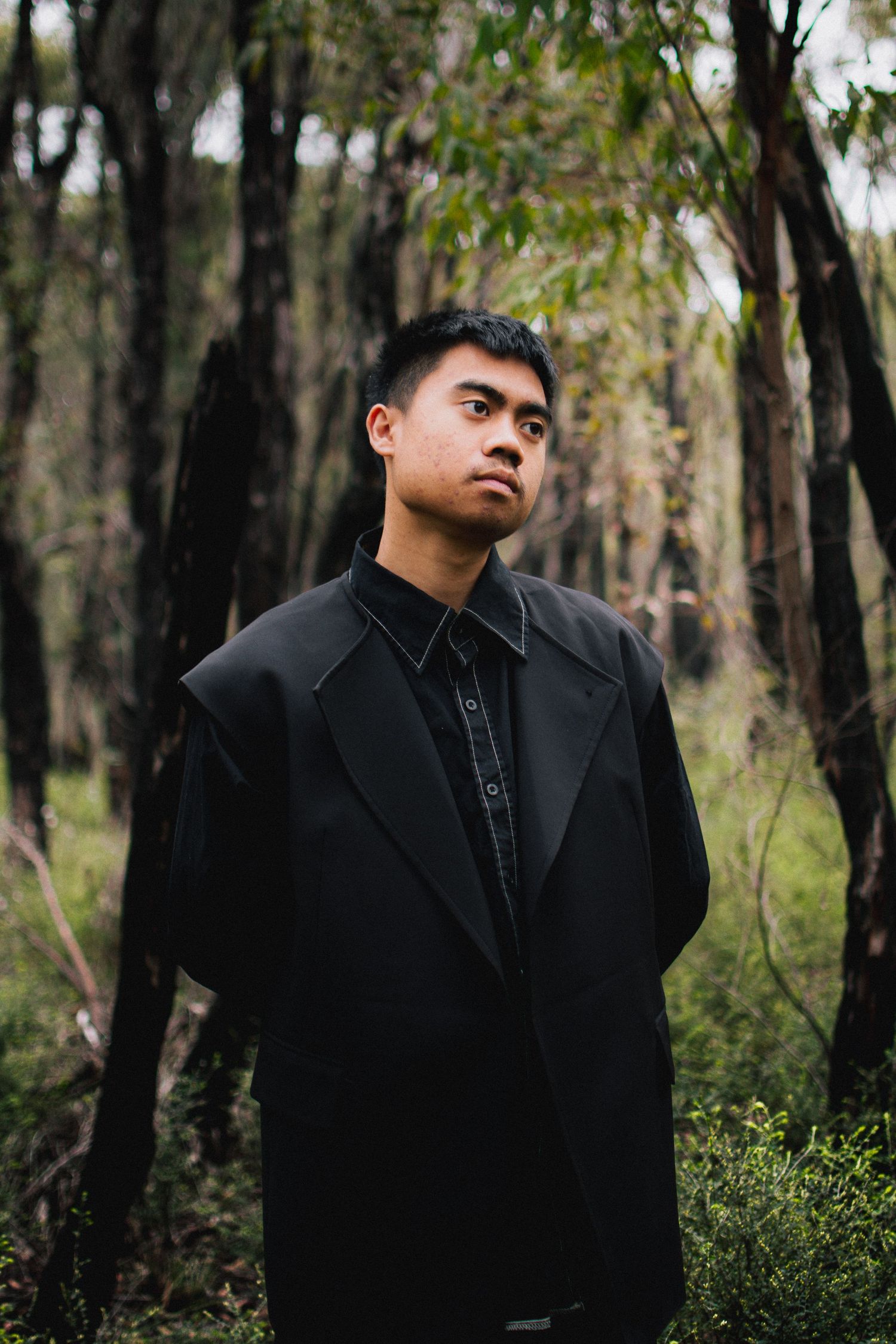 Dramatic portrait of person in black coat standing in misty forest setting.
