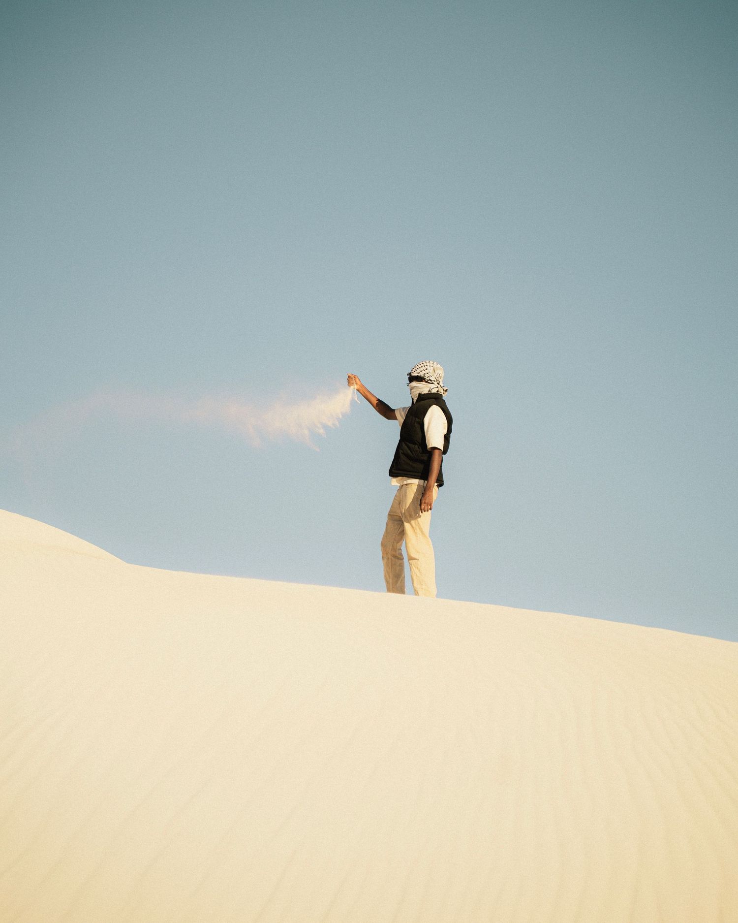 Figure throwing sand on desert dune creating a dramatic silhouette against clear sky.