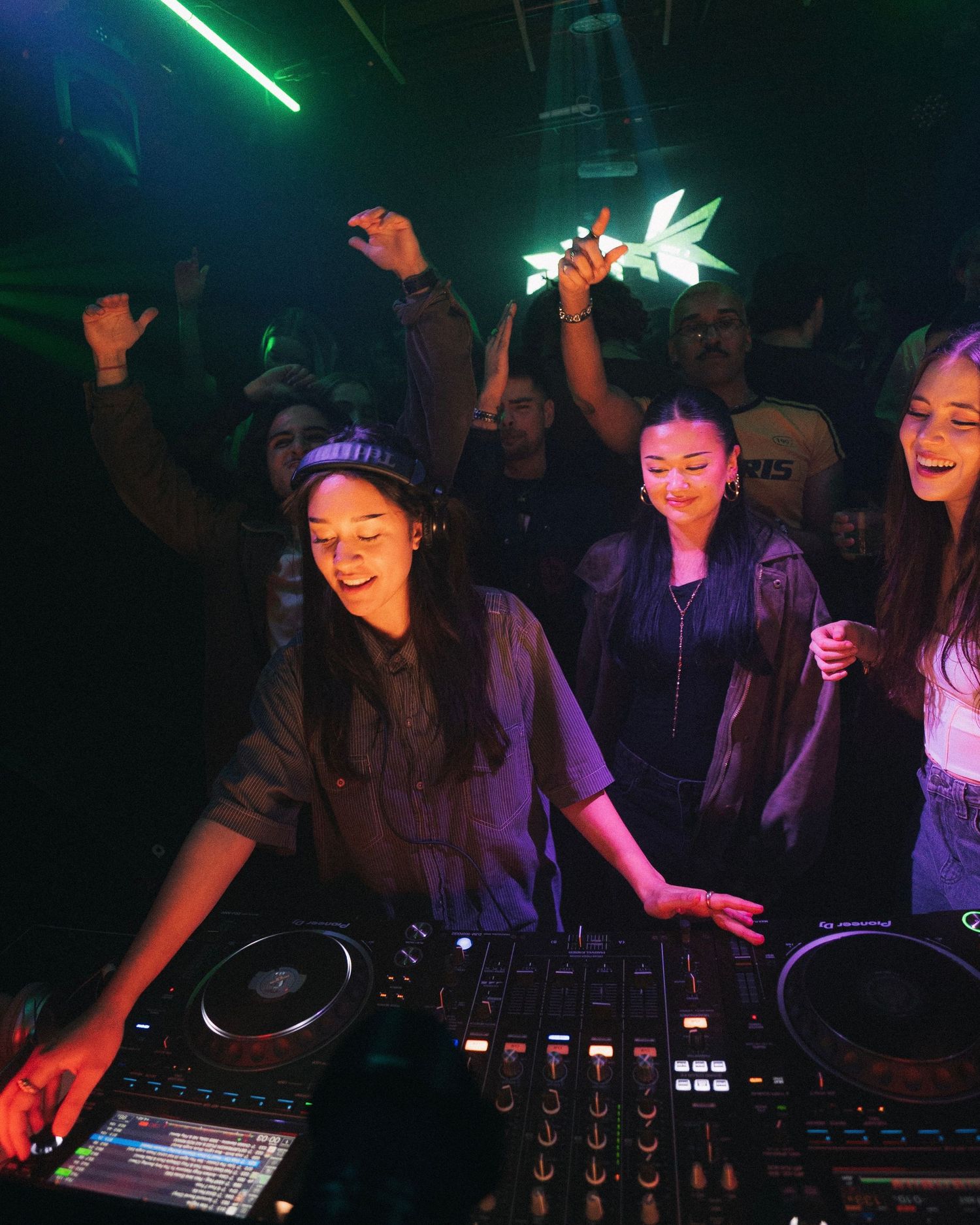 DJs performing at colorful nightclub with green lighting and crowd dancing.