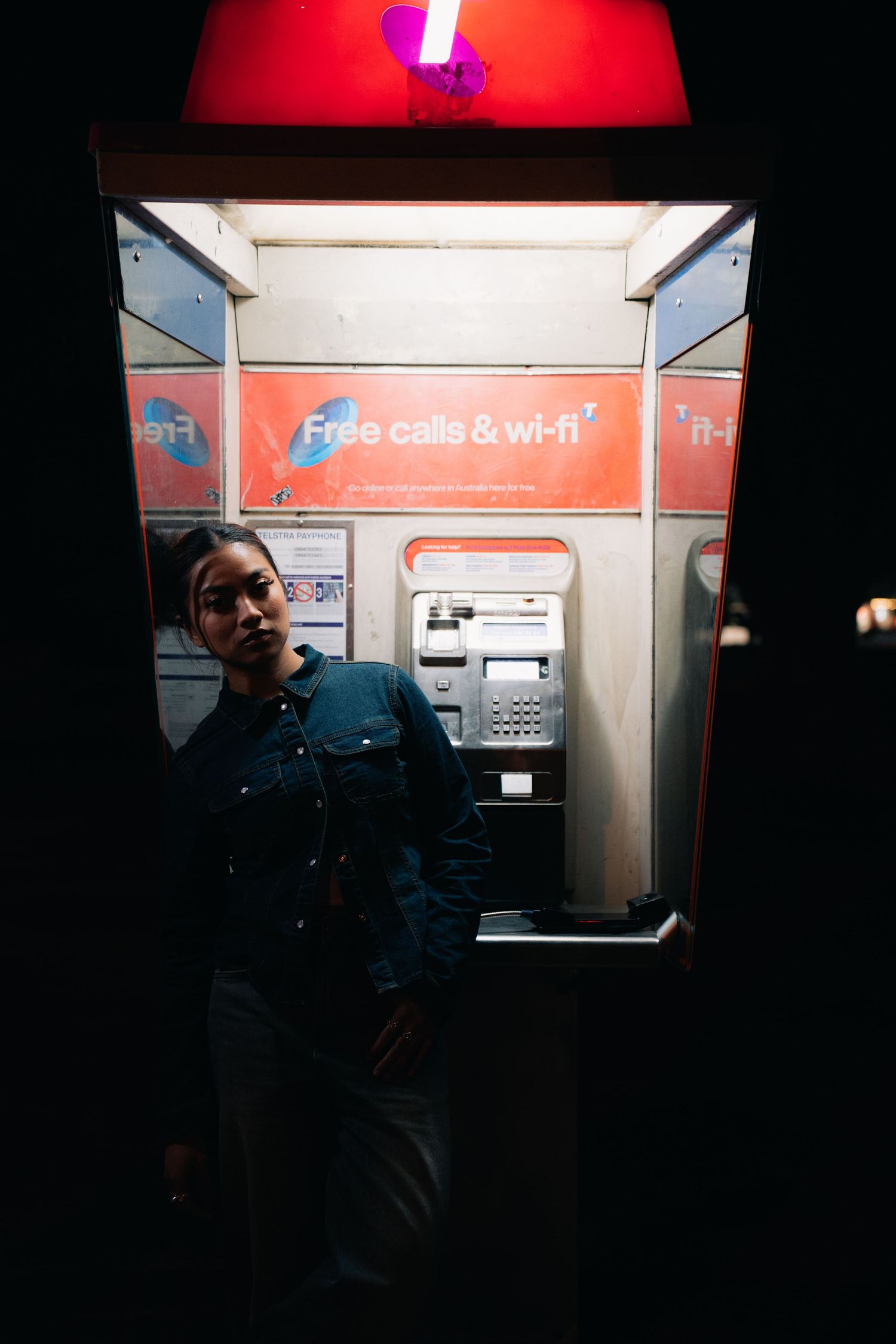 Dimly lit payphone booth interior with orange 'Free calls & wi-fi' sign and illuminated red light above.