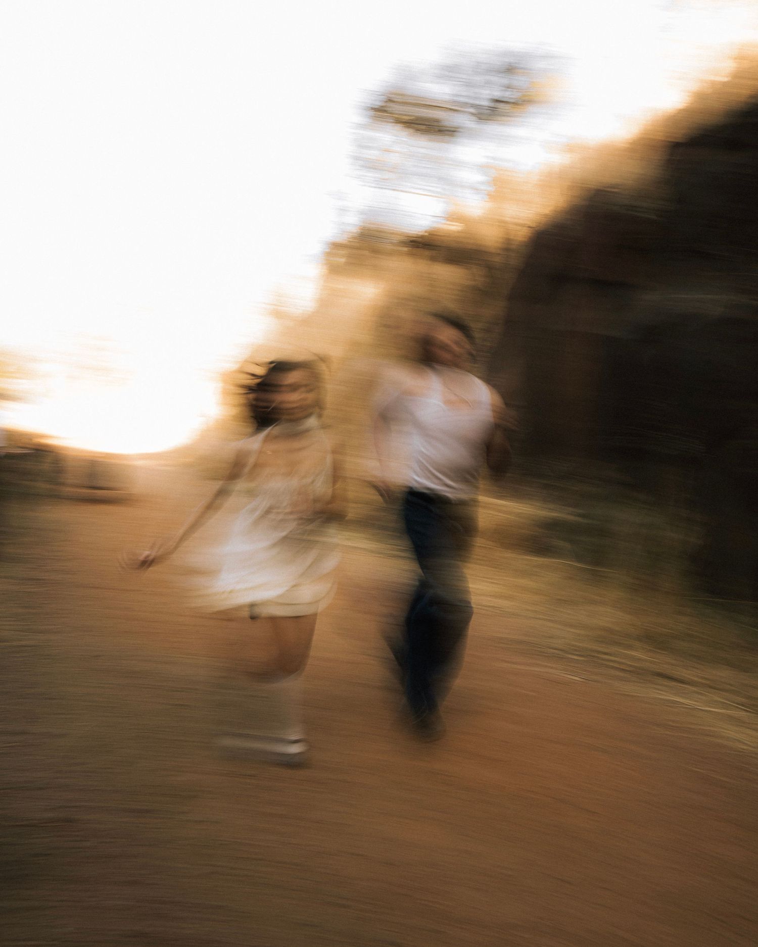 Motion-blurred artistic photograph of two figures dancing or moving in soft golden lighting outdoors.
