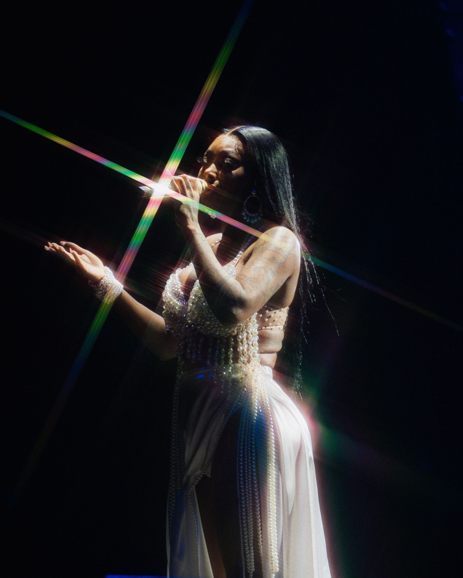 Artist in sparkly dress performing on stage with colorful light effects.
