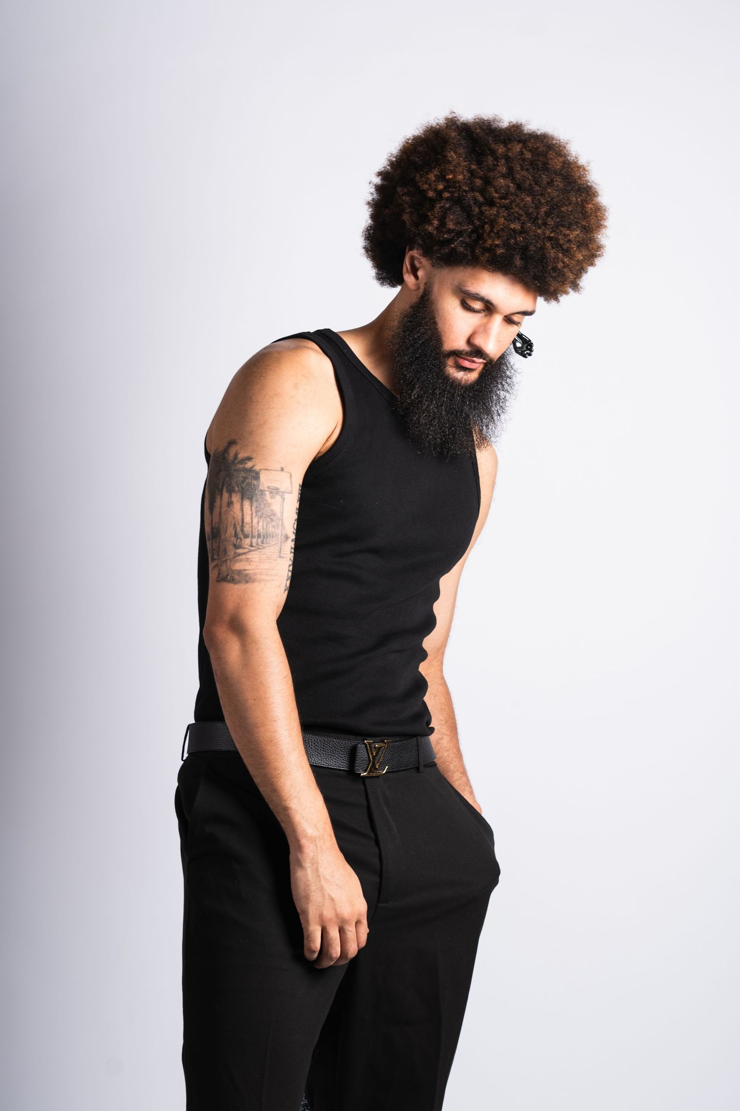 Person with a natural curly afro hairstyle wearing a black sleeveless top poses stylishly against a light background.