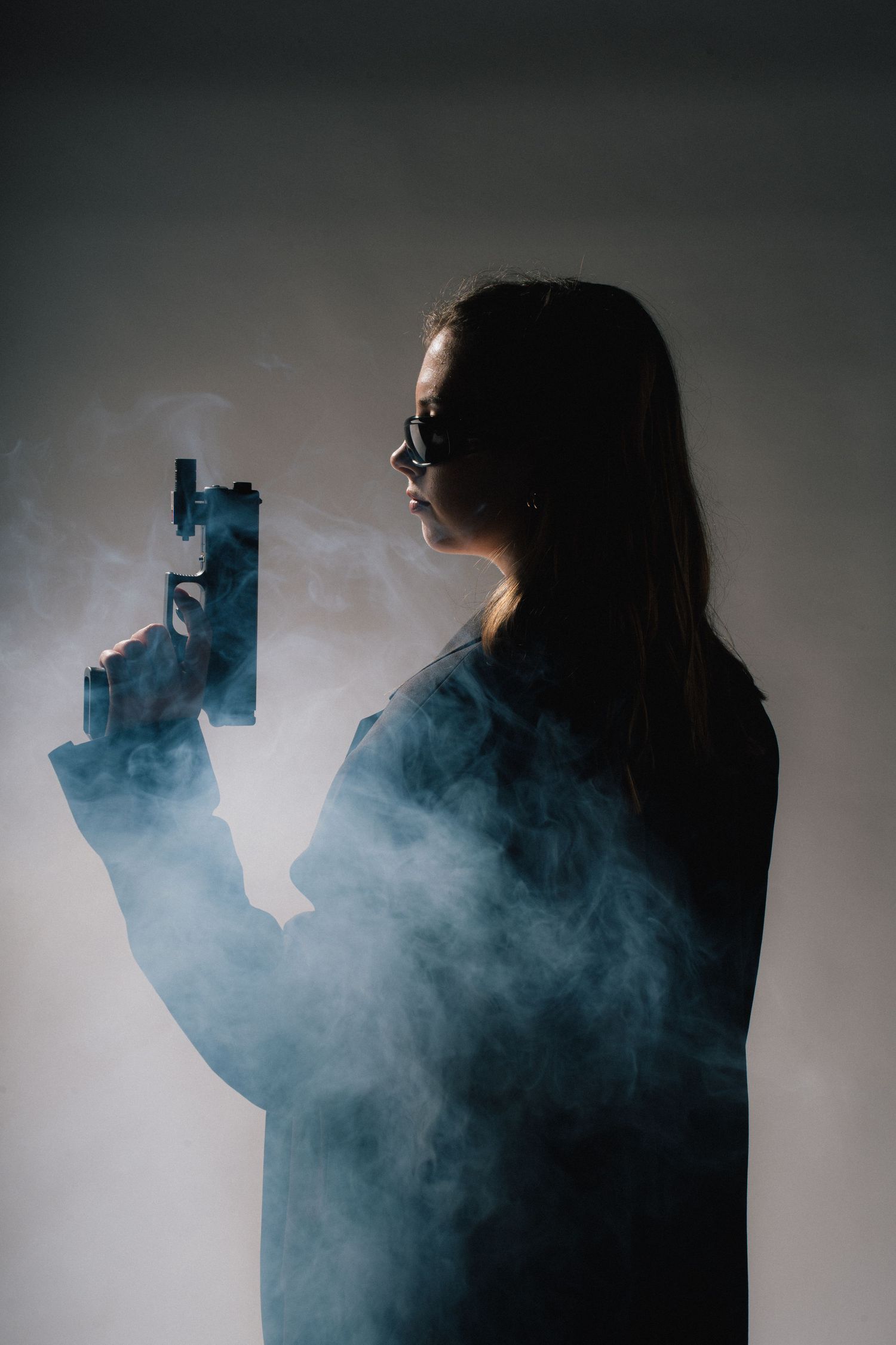 Dramatic silhouette of figure holding gun enveloped in blue smoke against white background.