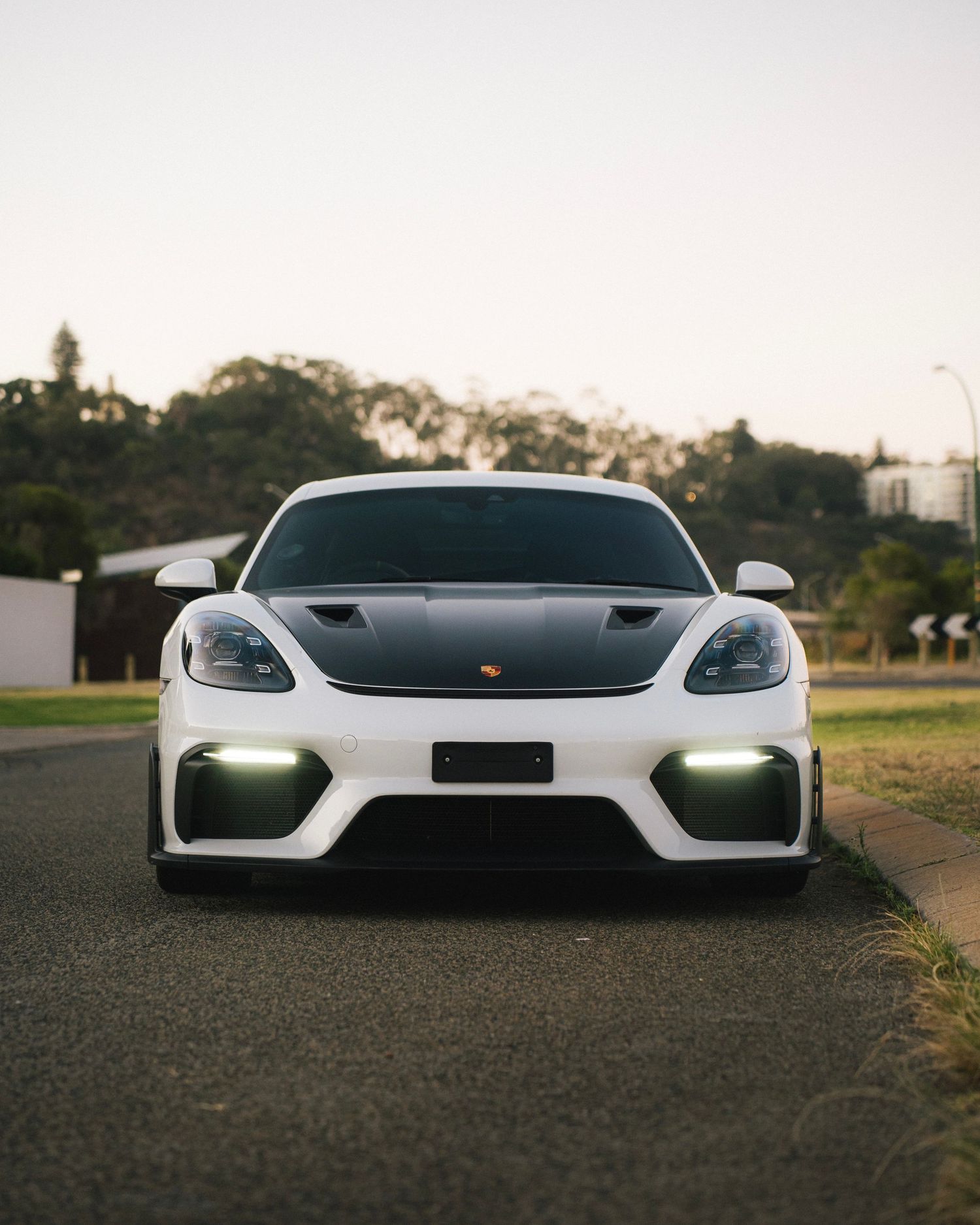 Front view of a white Porsche sports car with LED running lights on a road at dusk.