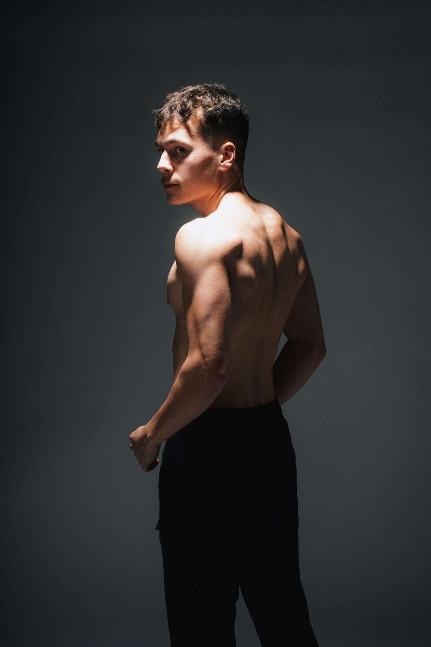 Dramatic studio portrait showing a muscular physique against a dark background.