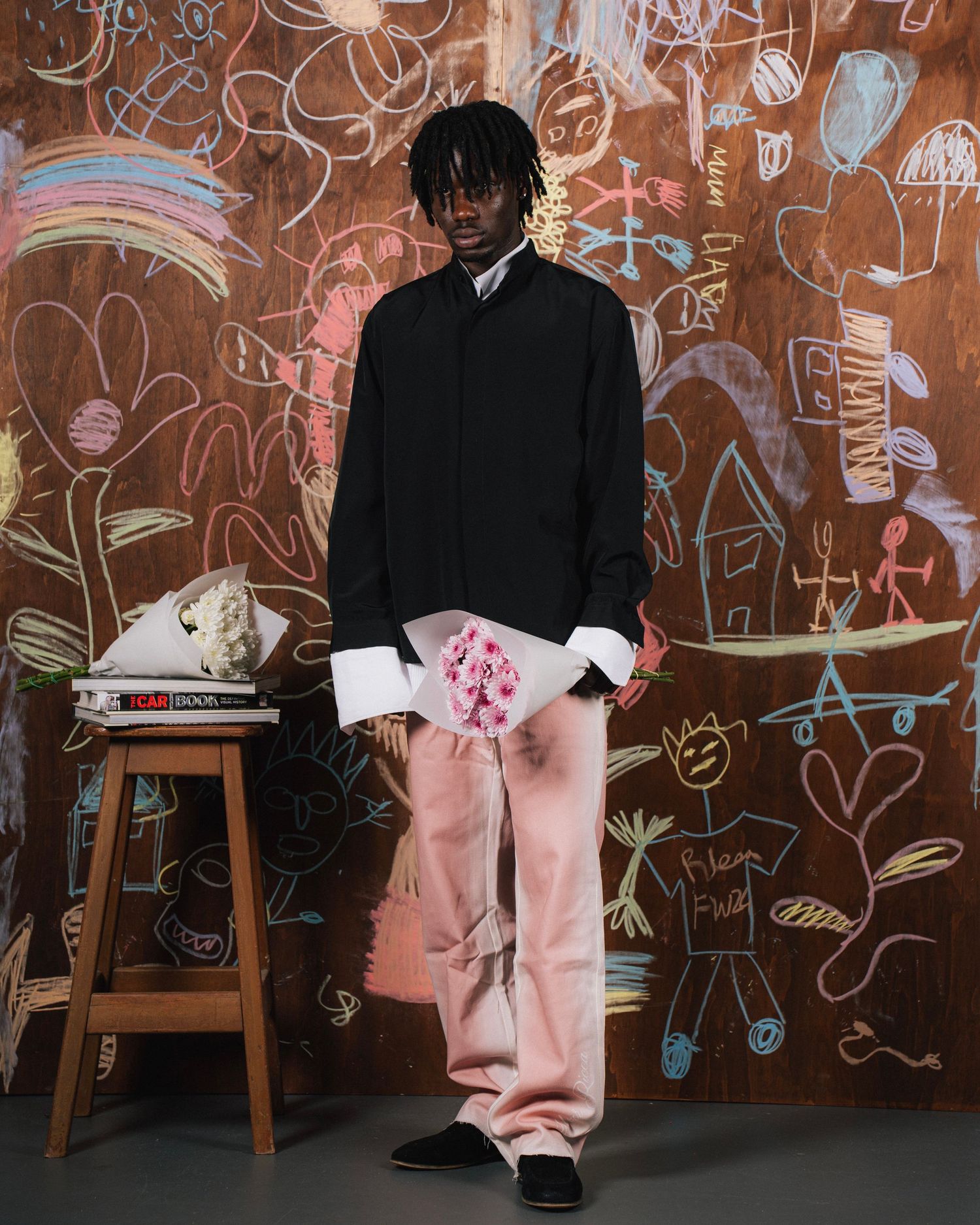 Fashion model in black sweater and pink pants posing against colorful graffiti wall.