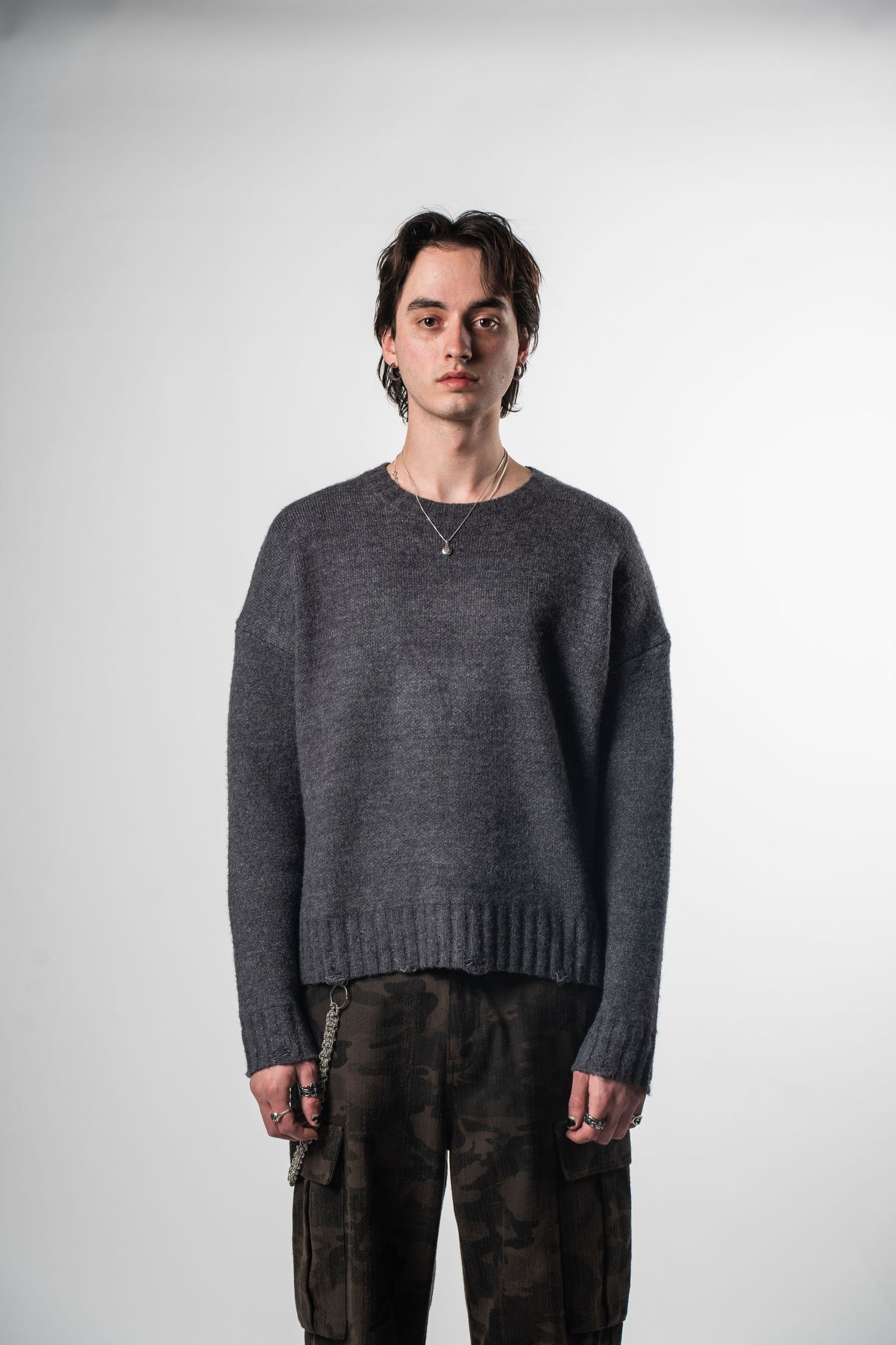Model in dark gray knit sweater and camouflage cargo pants against white background.