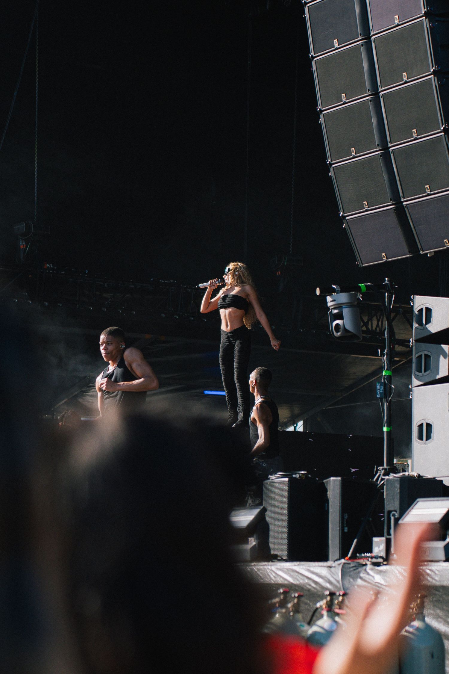 Musical performance on dark stage with large speaker array visible in the background at a concert venue.