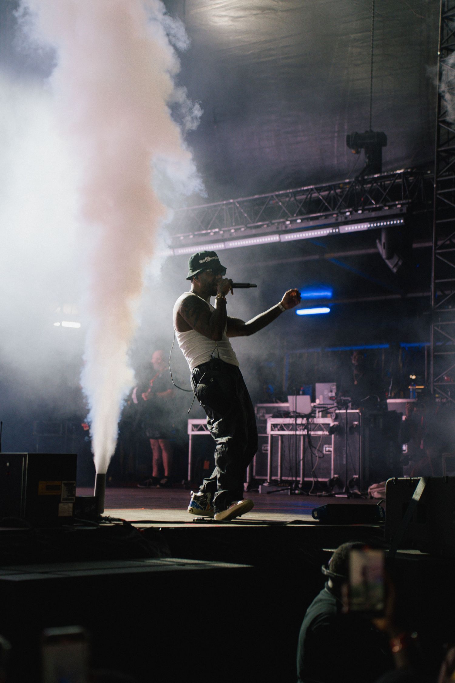 Concert performer silhouetted on stage with dramatic fog effects and blue lighting during a live music performance.