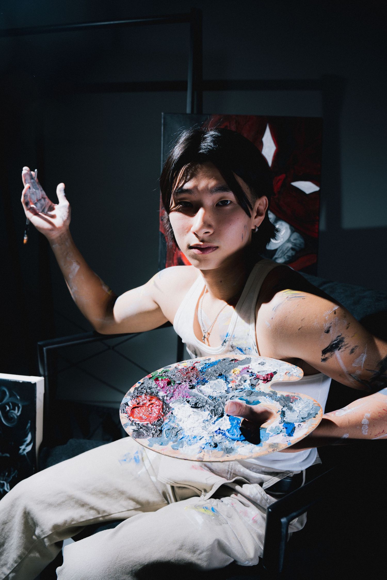 Artist working with paint and holding small sculpture in a dimly lit studio space.