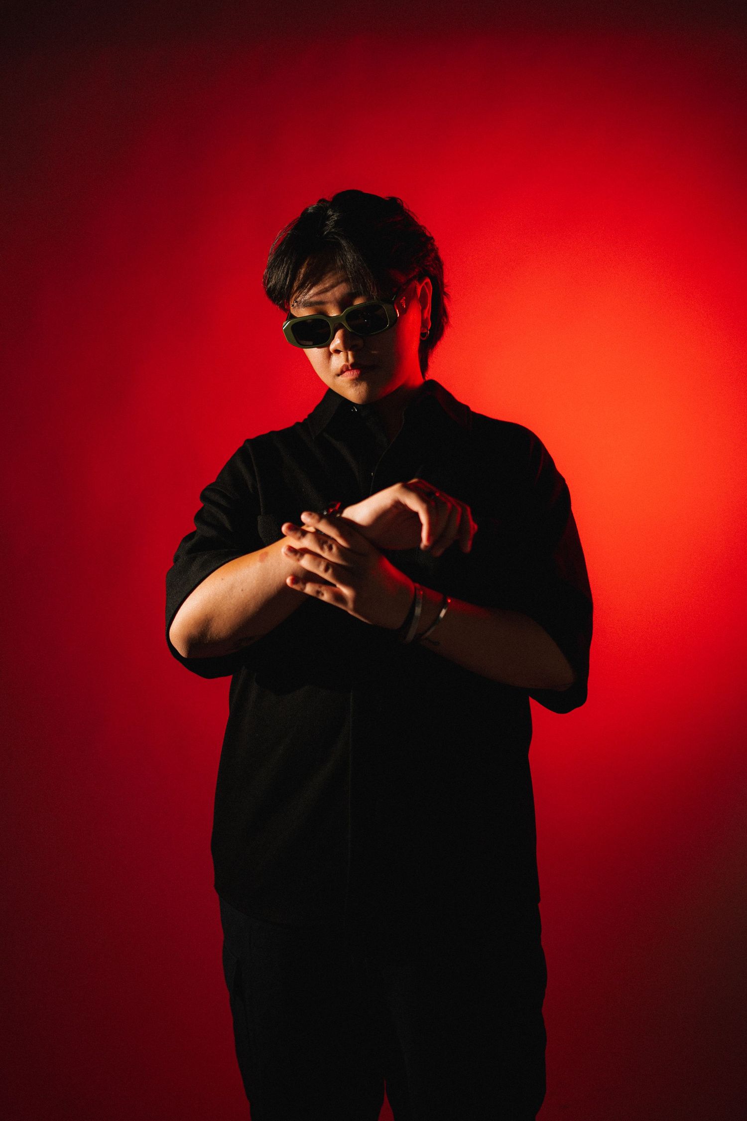 Dramatic silhouette of figure wearing sunglasses and black clothing against vibrant red background with moody lighting.