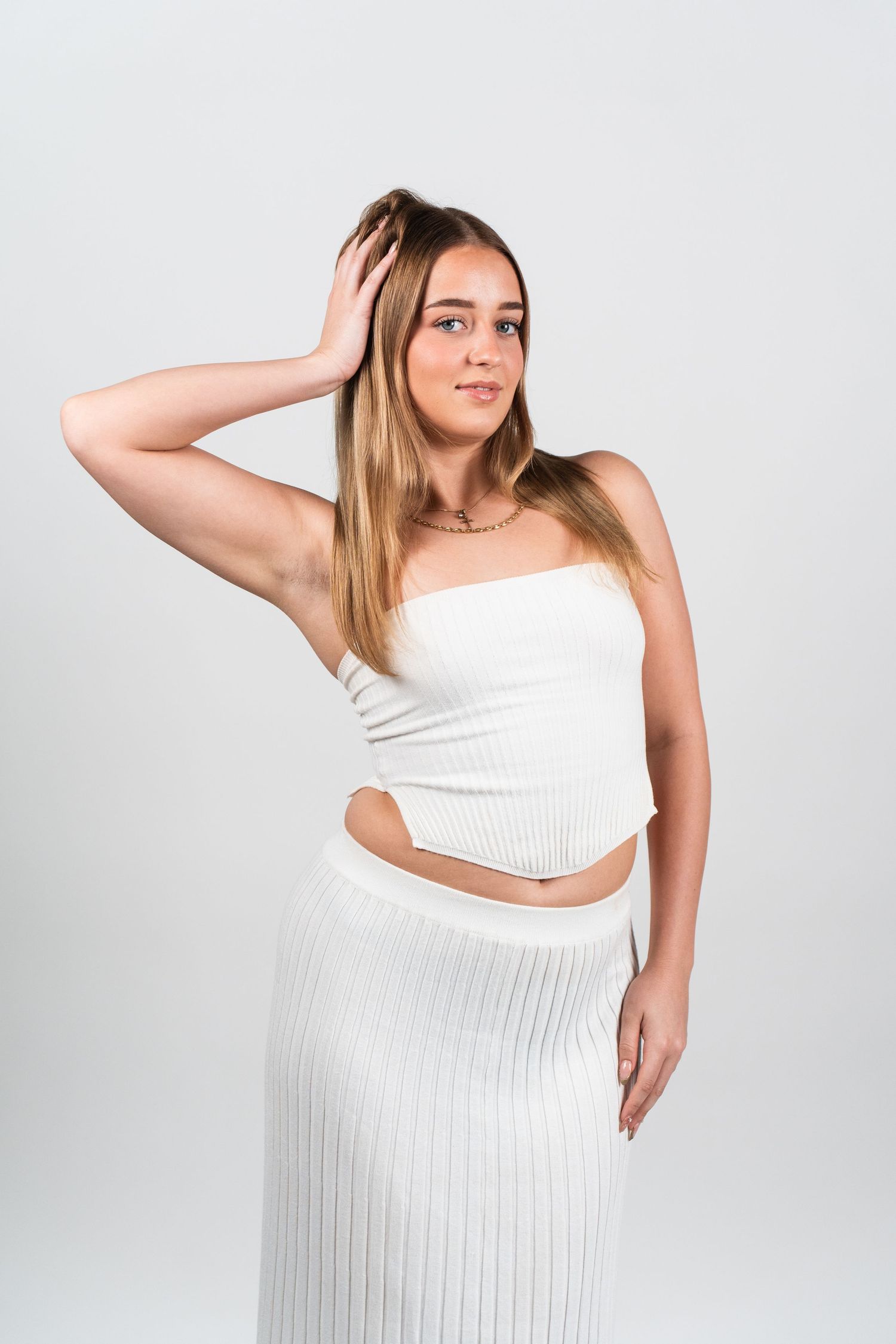 Model in a white pleated dress poses gracefully against a light background in a four-panel fashion series.