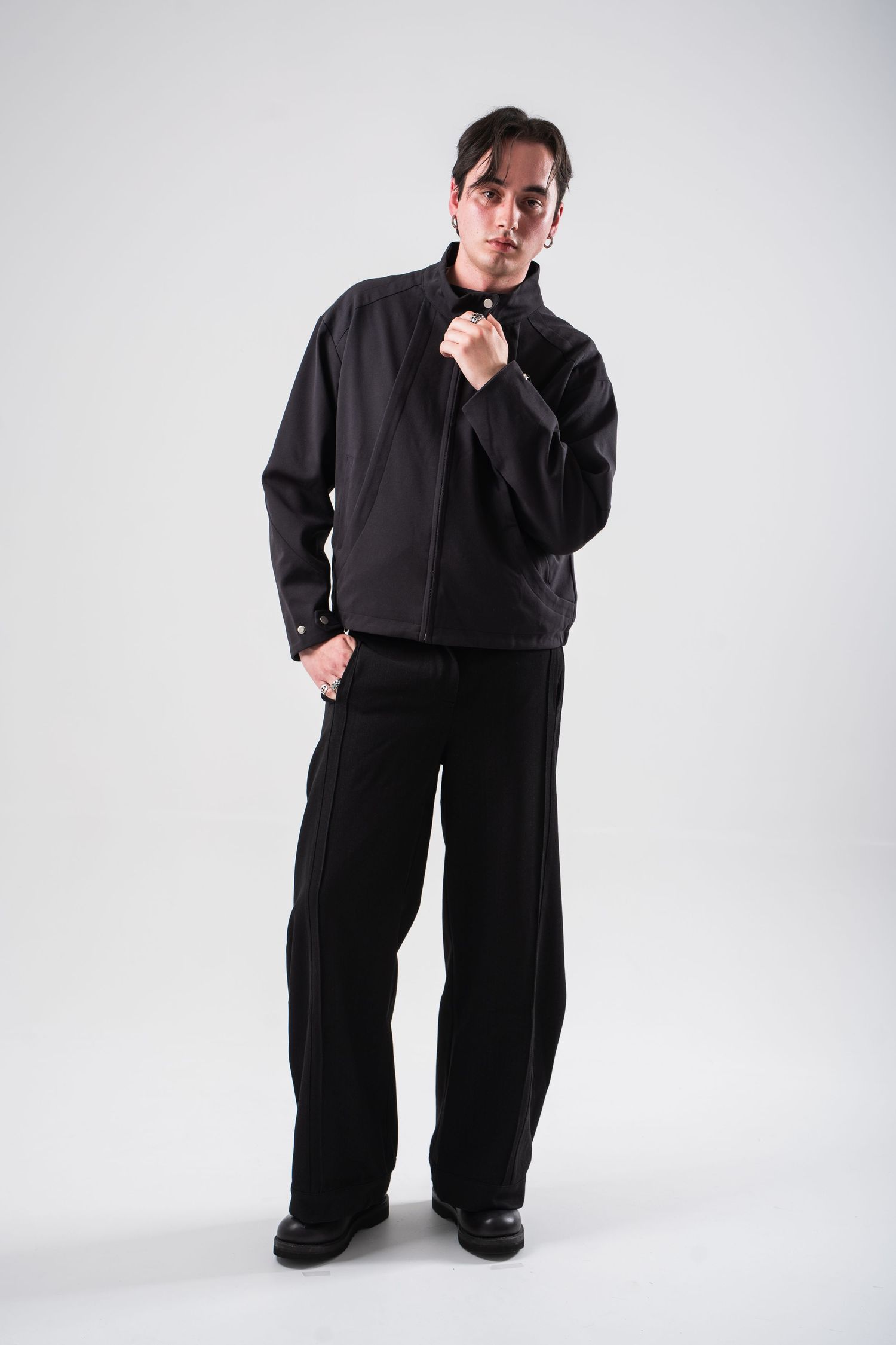 Model wearing oversized black ensemble strikes dramatic poses against white backdrop in fashion photoshoot series.