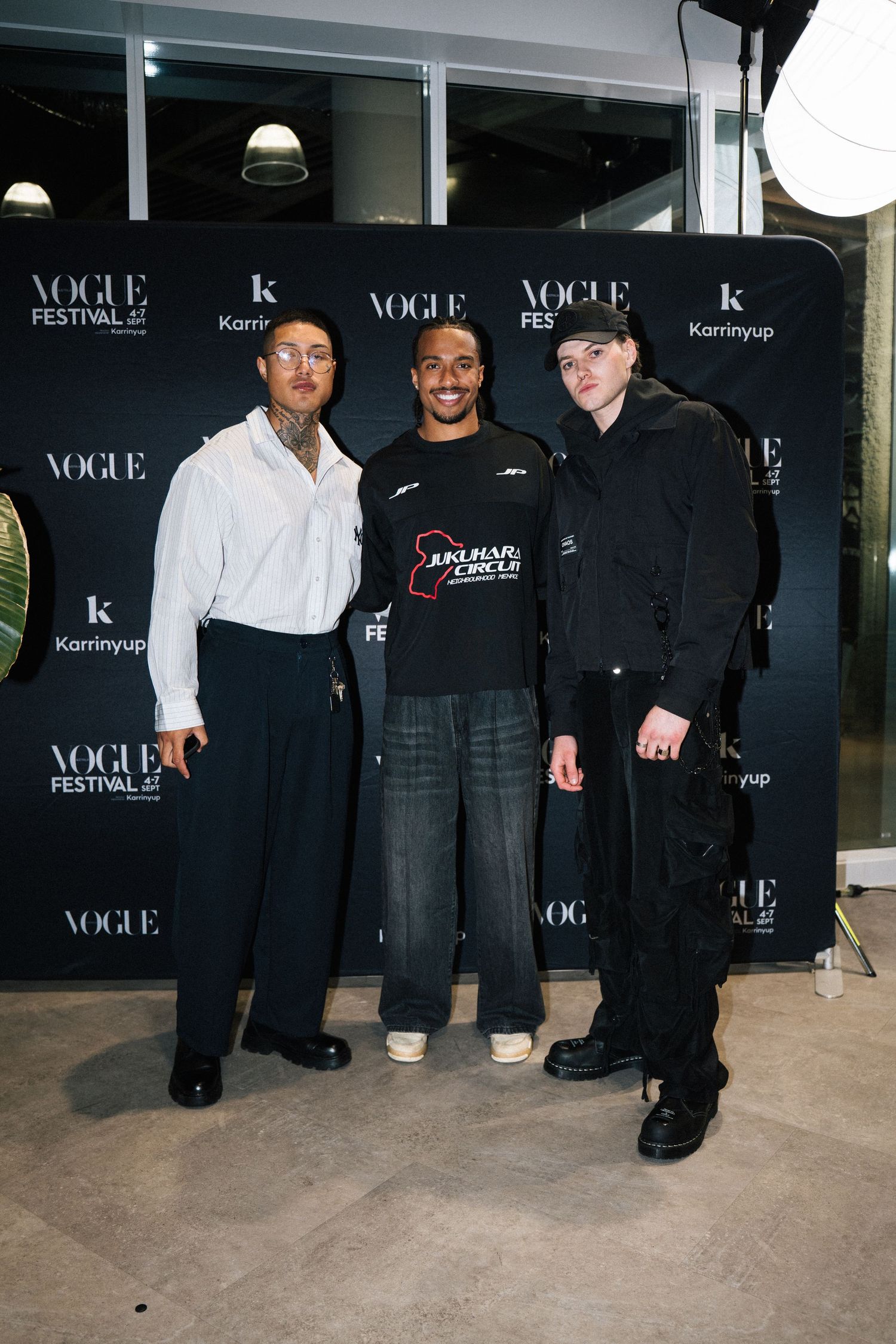 Three people pose together against a backdrop with Vogue Festival and K branding at an event.
