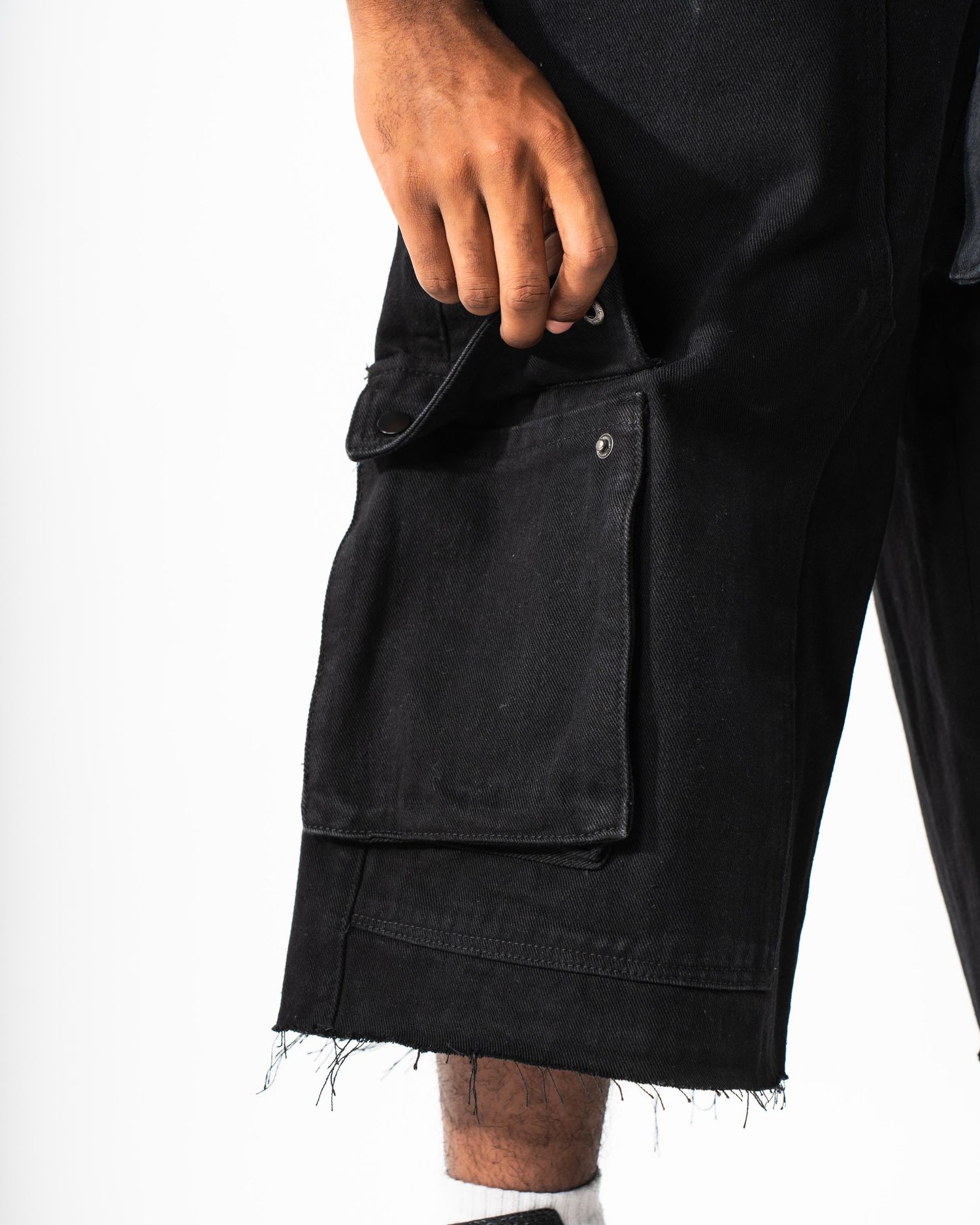 Close-up of black cargo shorts pocket with distressed hem detail.