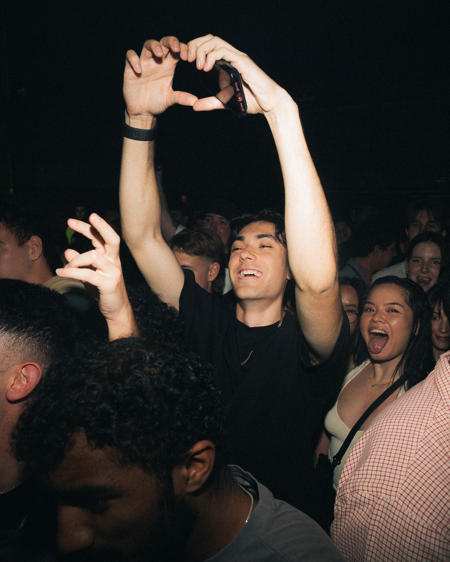 Concert attendee making heart shape gesture while enjoying music in crowded venue.