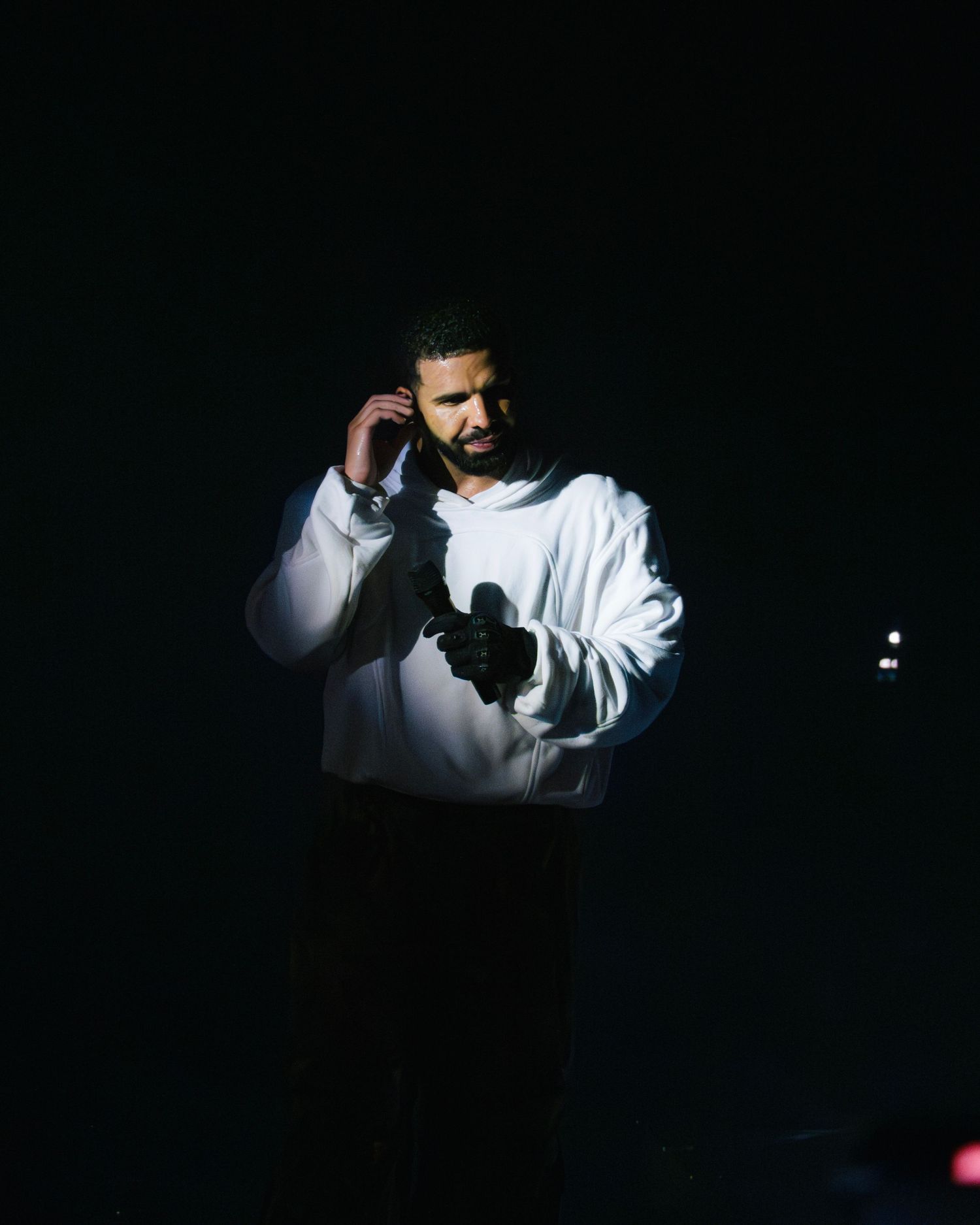 Person in a white sweater stands in dramatic lighting against a dark background while using a phone.