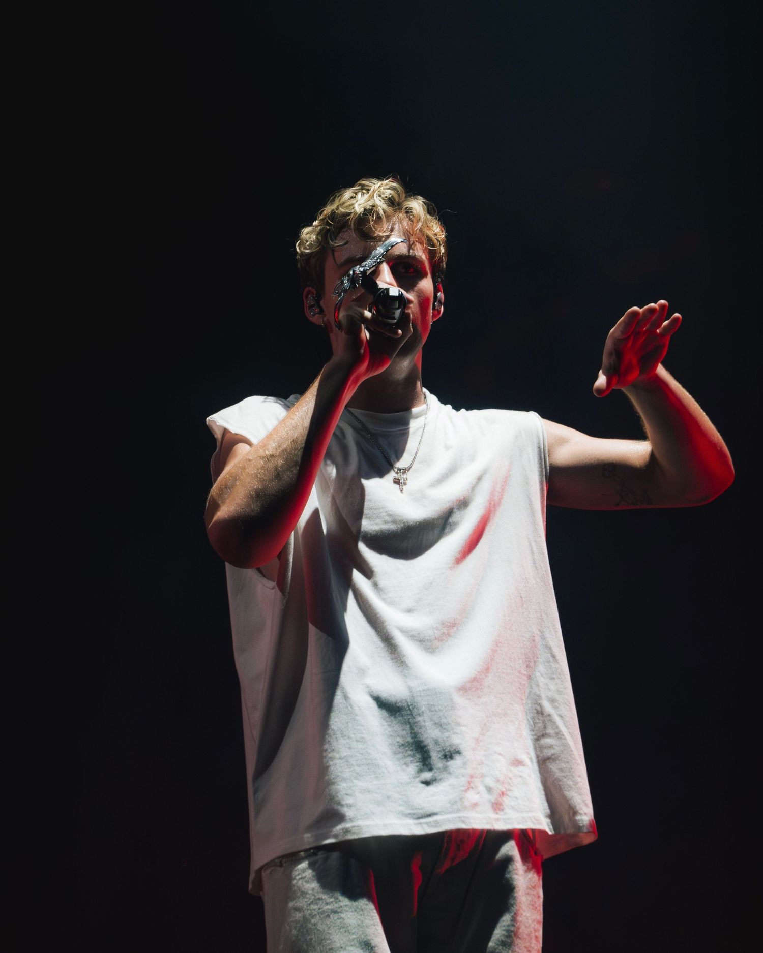 A performer in a white t-shirt with red liquid dripping down stands dramatically on a dark stage.