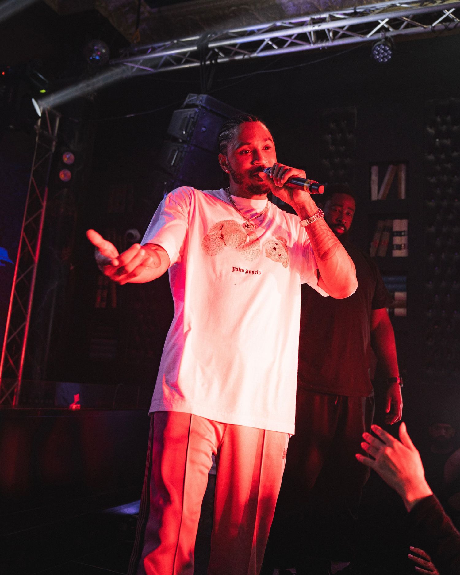 Performer in white t-shirt singing on stage with red lighting effects.